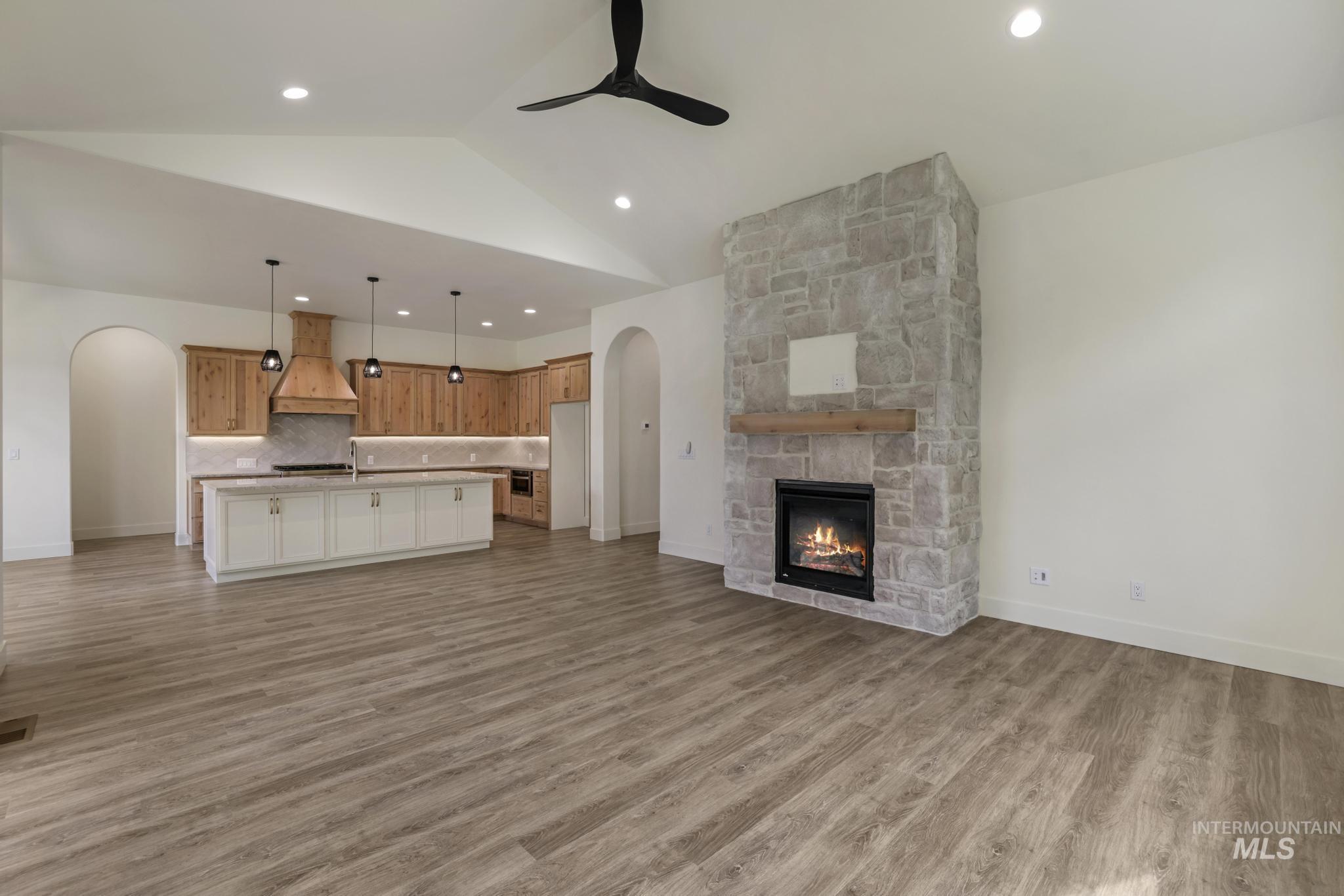 Unfurnished living room featuring arched walkways, light wood finished floors, a fireplace, lofted ceiling, and a ceiling fan