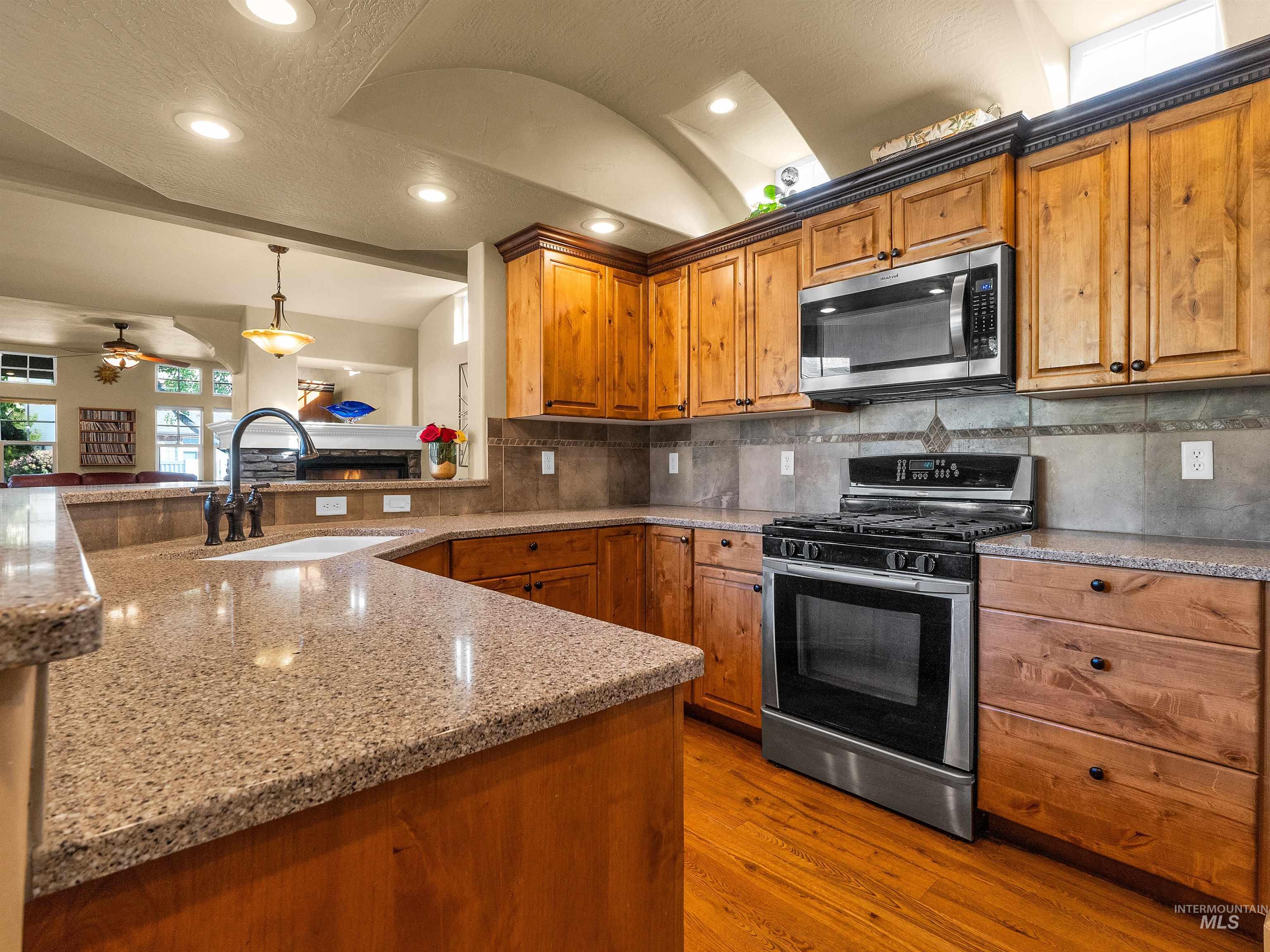 Kitchen with appliances with stainless steel finishes, brown cabinets, light stone counters, dark wood finished floors, and decorative light fixtures
