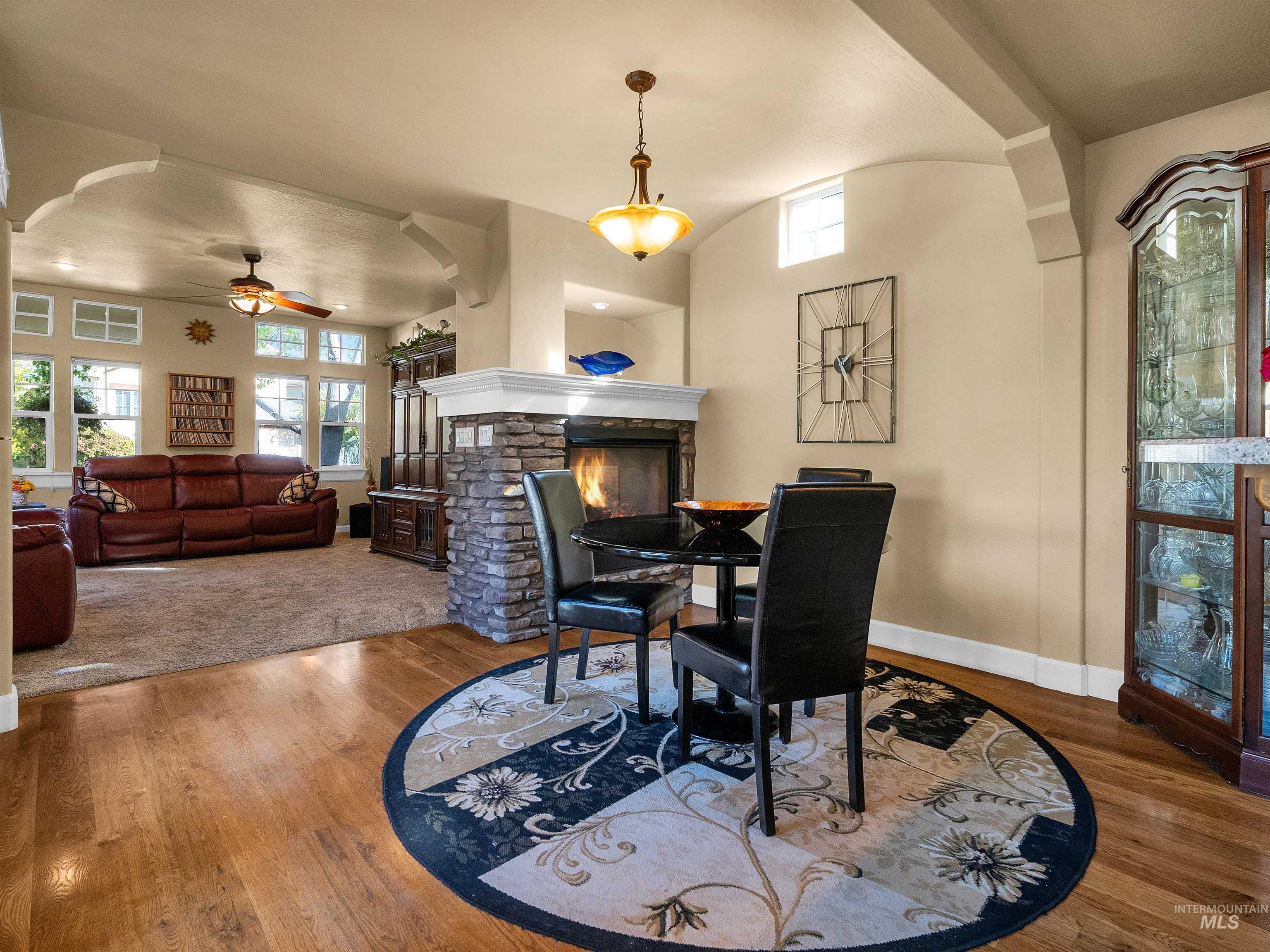 Dining room featuring wood finished floors, a ceiling fan, a stone fireplace, and arched walkways