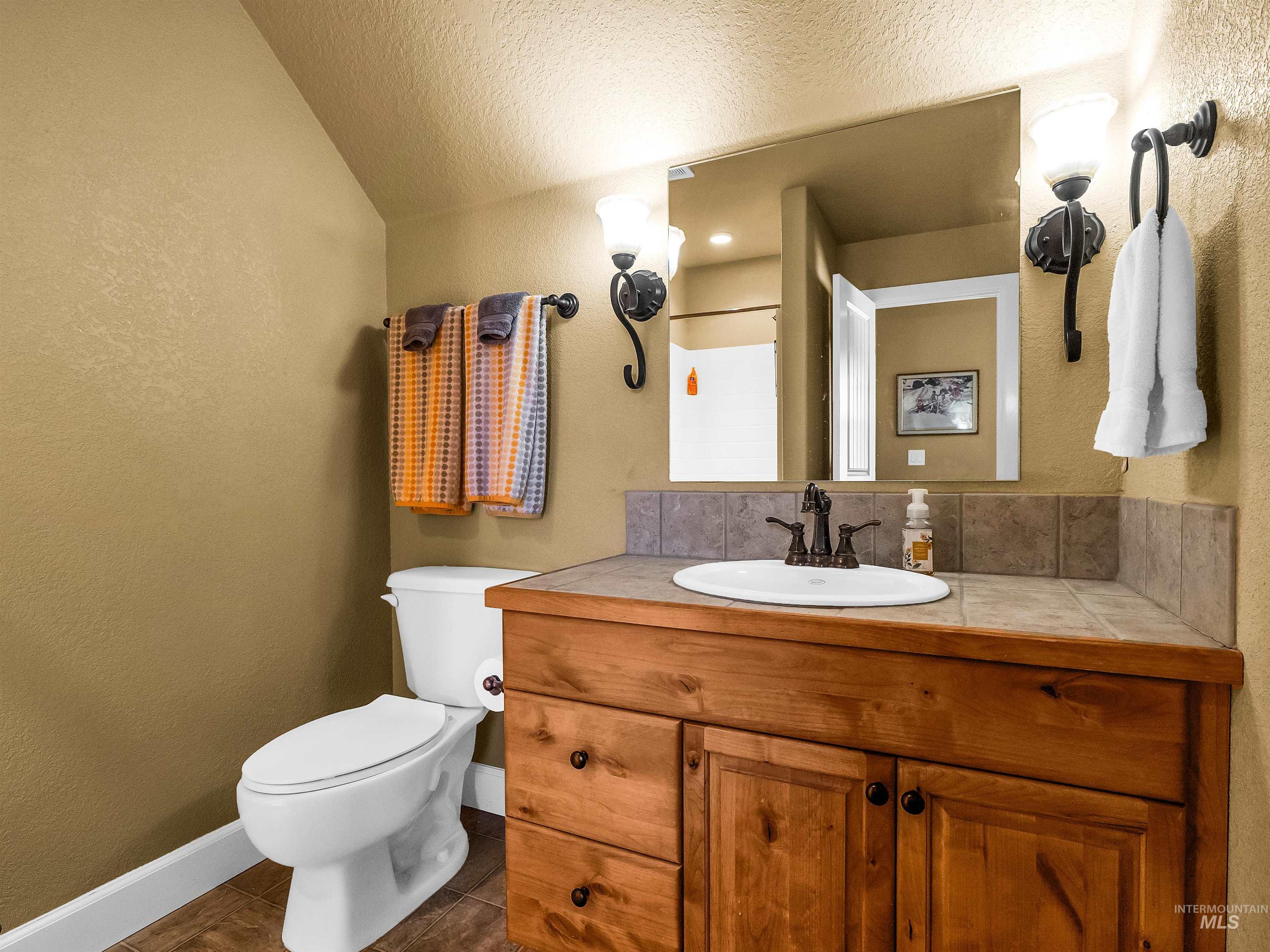 Bathroom featuring a textured wall, vanity, dark tile patterned flooring, a textured ceiling, and decorative backsplash