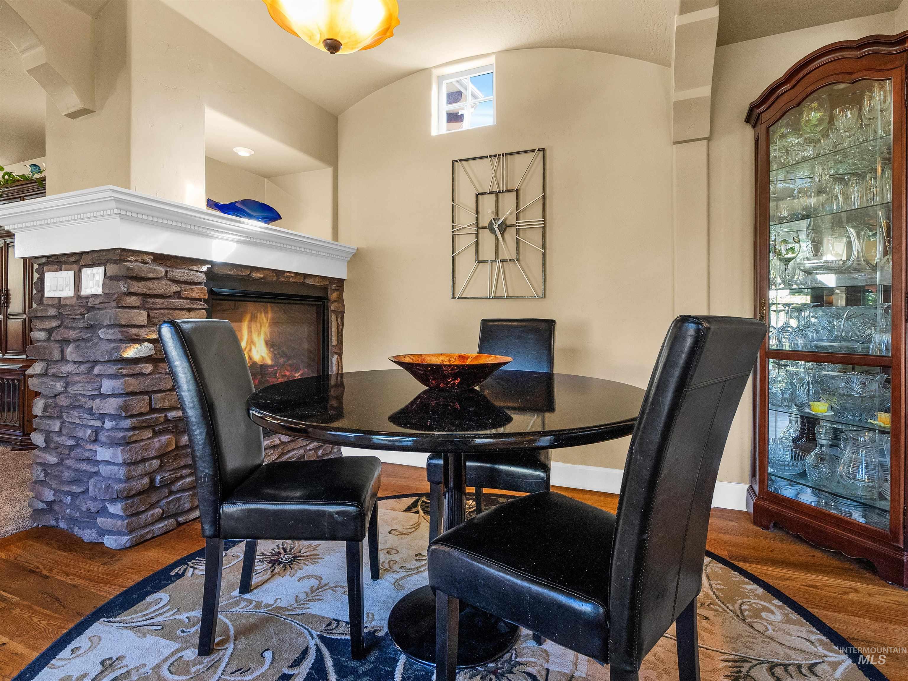 Dining room with wood finished floors, a stone fireplace, and vaulted ceiling
