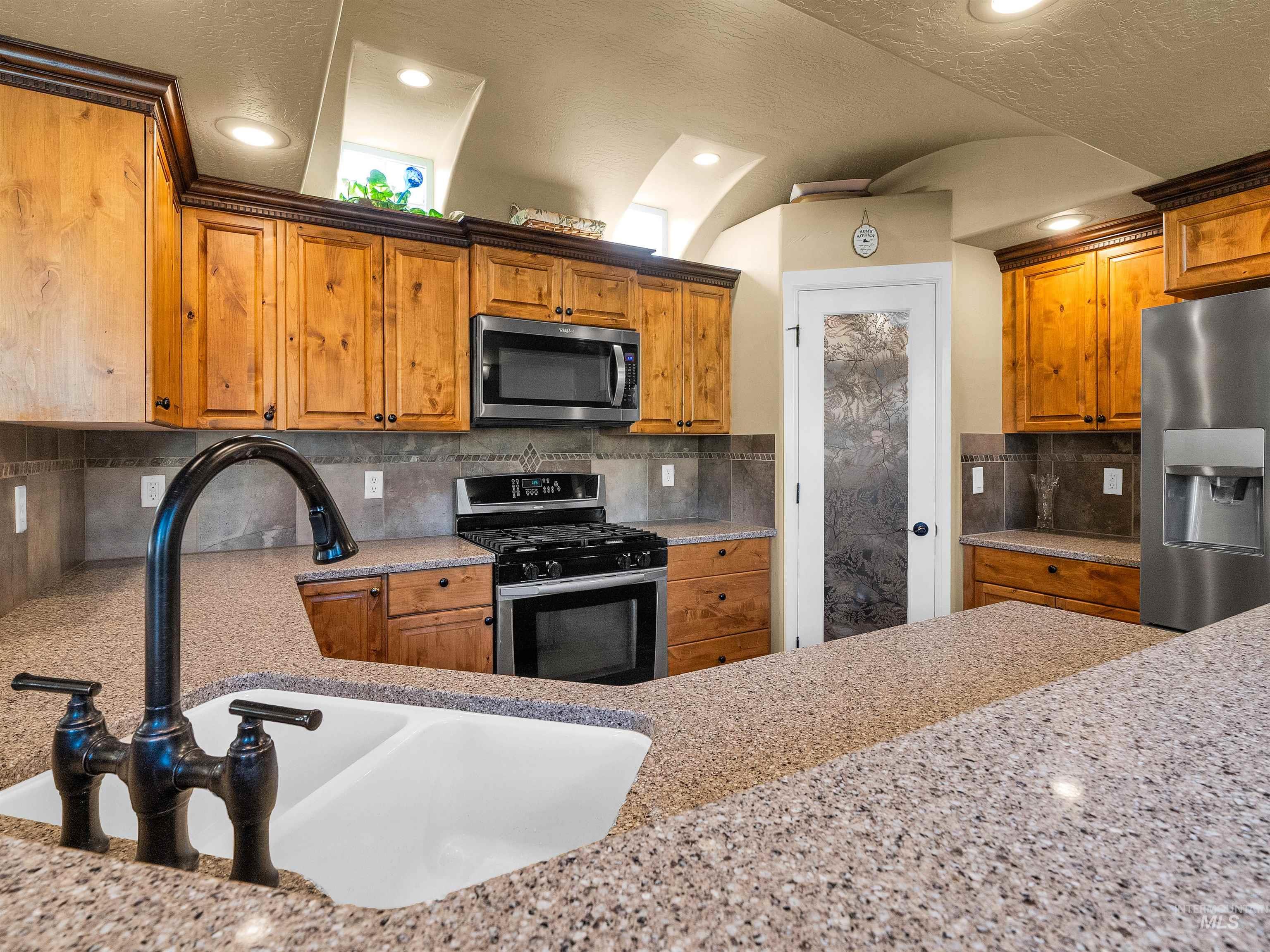 Kitchen with stainless steel appliances, brown cabinets, backsplash, recessed lighting, and light stone counters