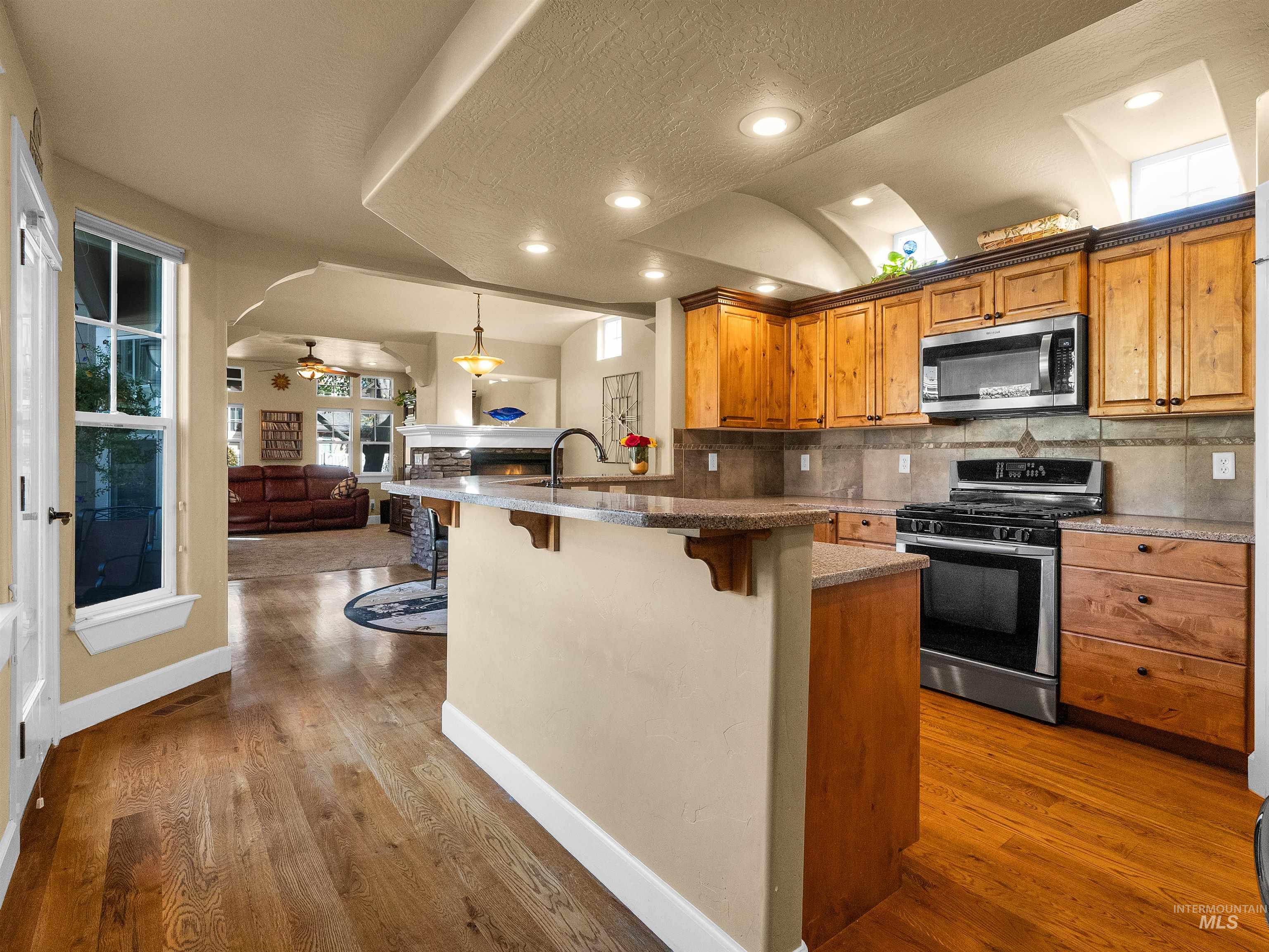 Kitchen with brown cabinetry, appliances with stainless steel finishes, decorative backsplash, a kitchen bar, and ceiling fan