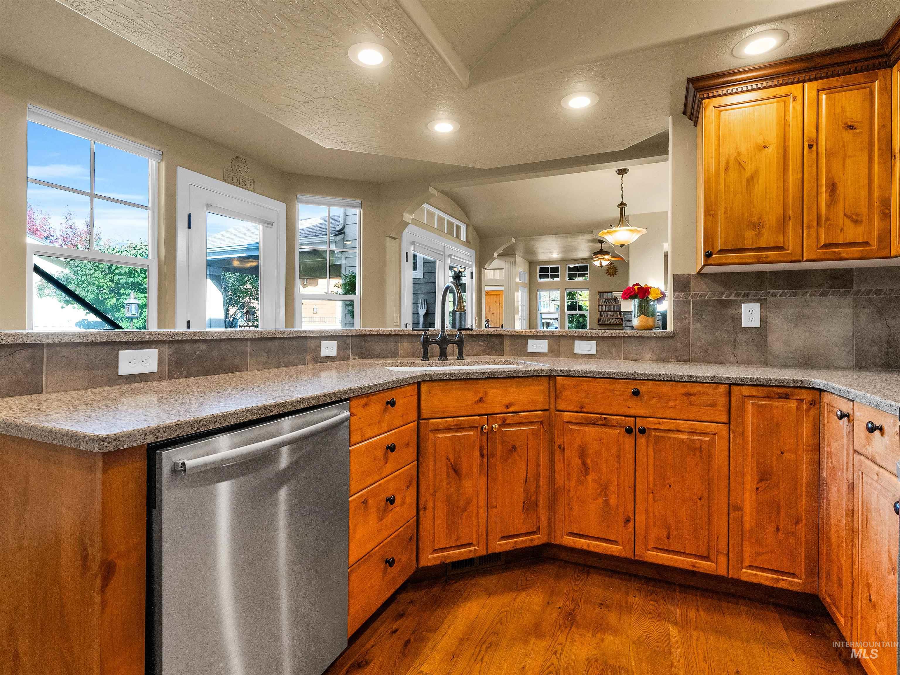 Kitchen featuring brown cabinetry, stainless steel dishwasher, dark wood-style floors, recessed lighting, and light stone counters