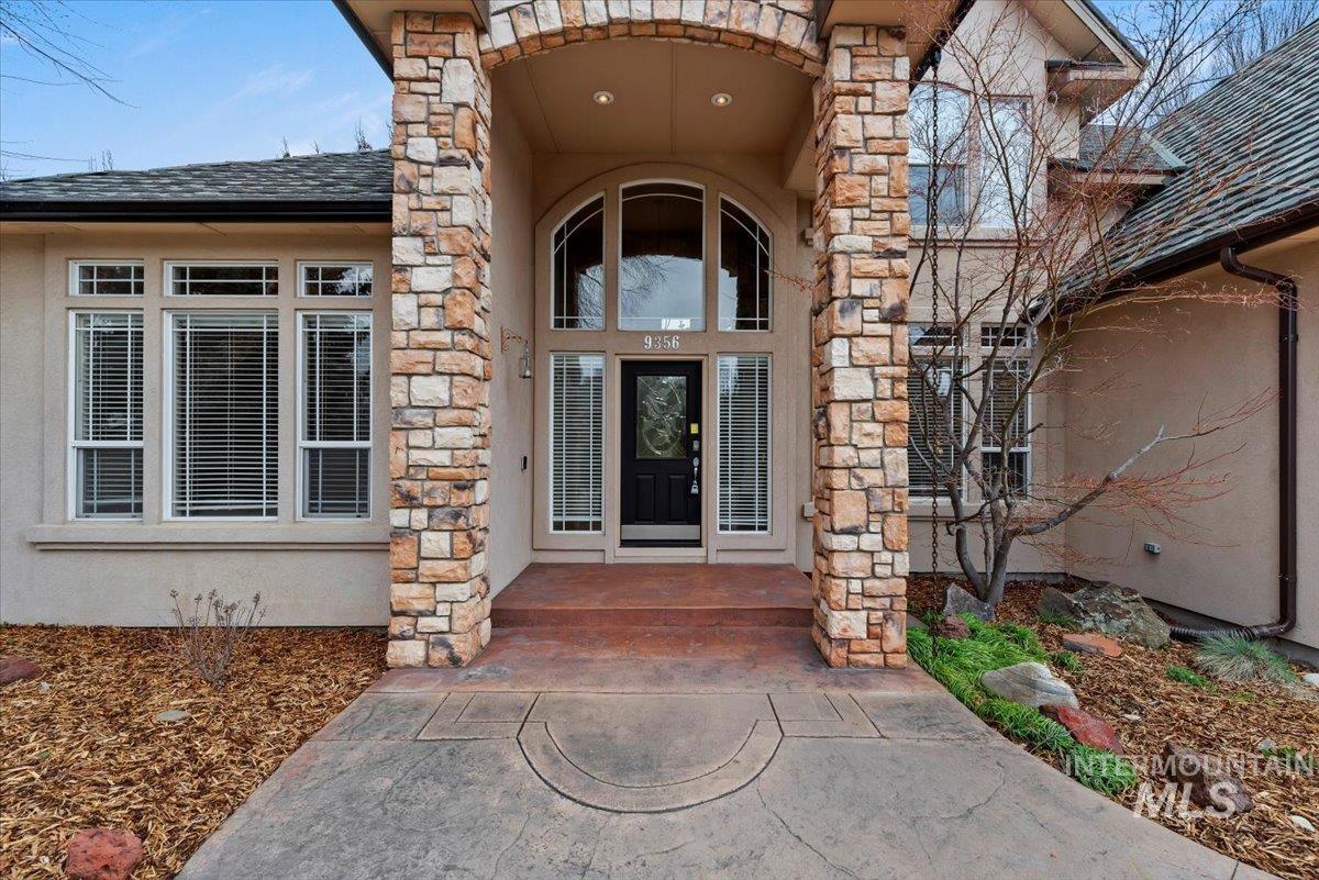 Entrance to property with stucco siding, stone siding, and roof with shingles