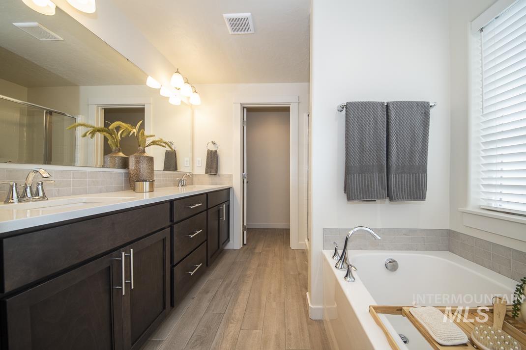 Bathroom featuring double vanity, a garden tub, an enclosed shower, light wood-style flooring, and a chandelier