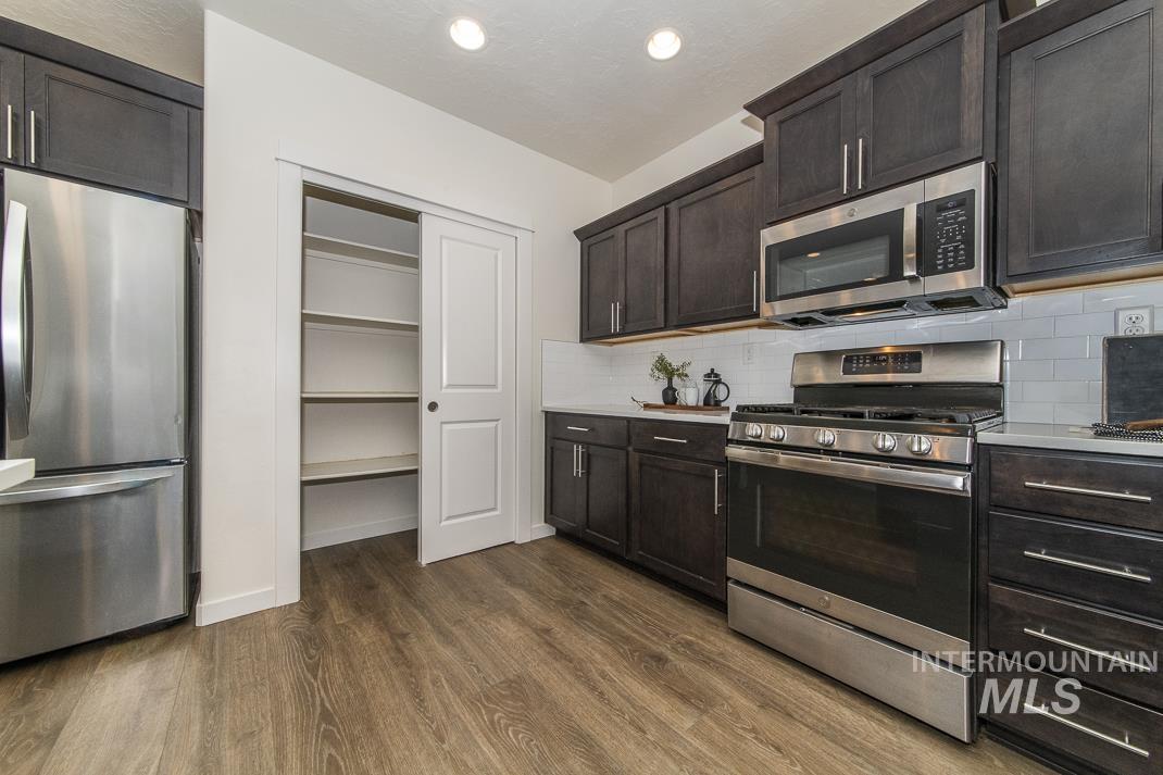 Kitchen featuring appliances with stainless steel finishes, dark brown cabinets, dark wood-style floors, and decorative backsplash