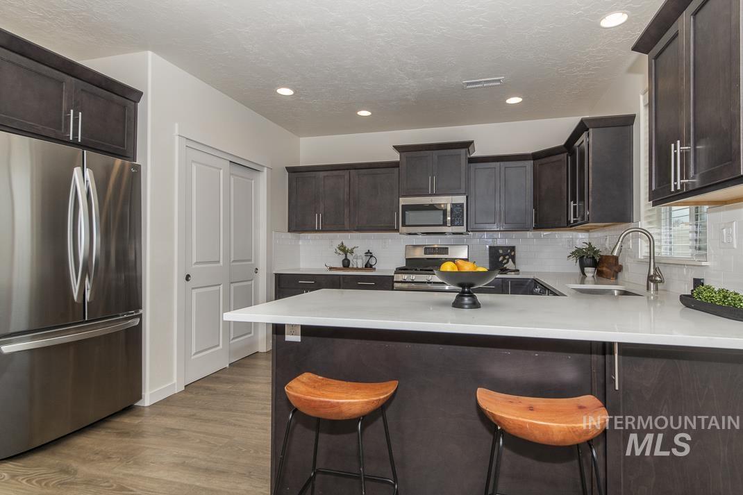 Kitchen featuring stainless steel appliances, dark brown cabinets, a breakfast bar area, light wood-style floors, and recessed lighting
