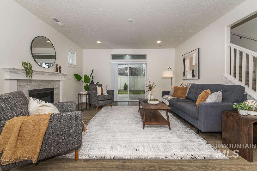 Living room featuring a brick fireplace, wood finished floors, stairs, and a textured ceiling
