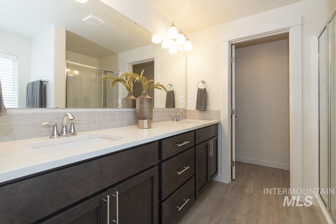 Bathroom featuring a shower stall, double vanity, light wood-style flooring, and tasteful backsplash