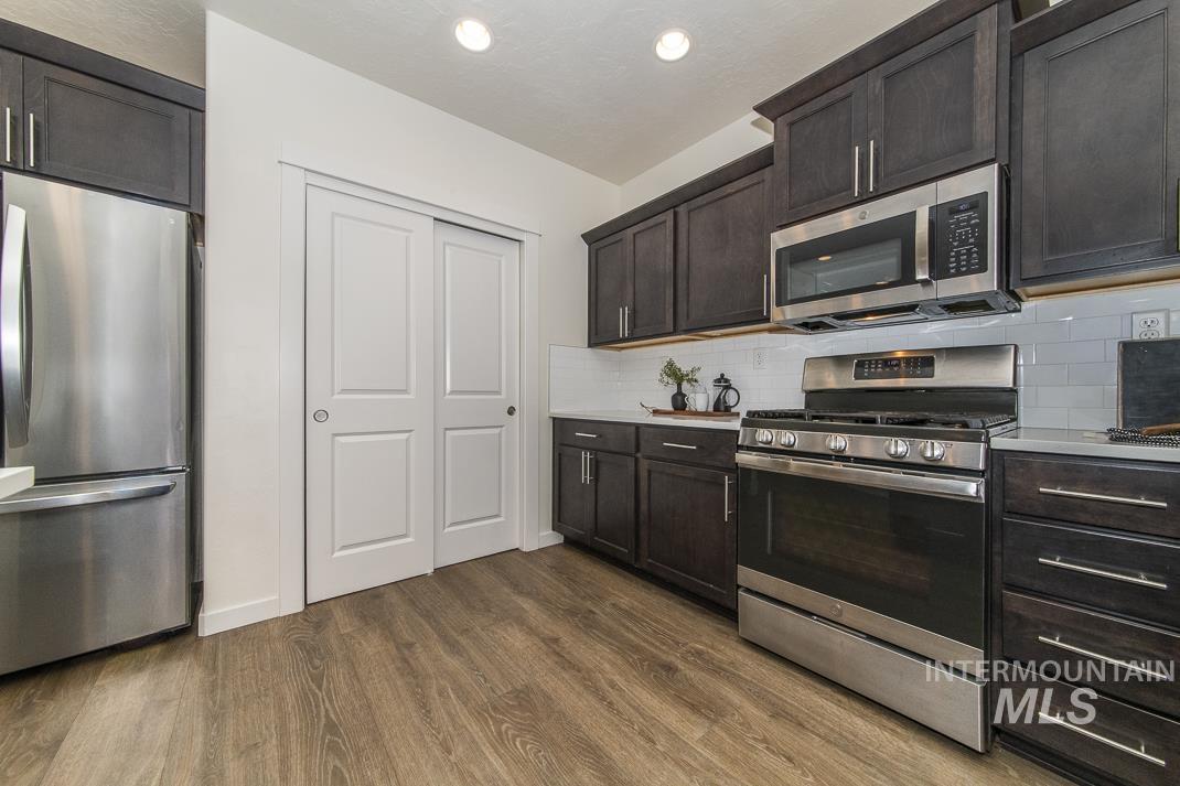 Kitchen with appliances with stainless steel finishes, dark brown cabinetry, dark wood finished floors, and tasteful backsplash