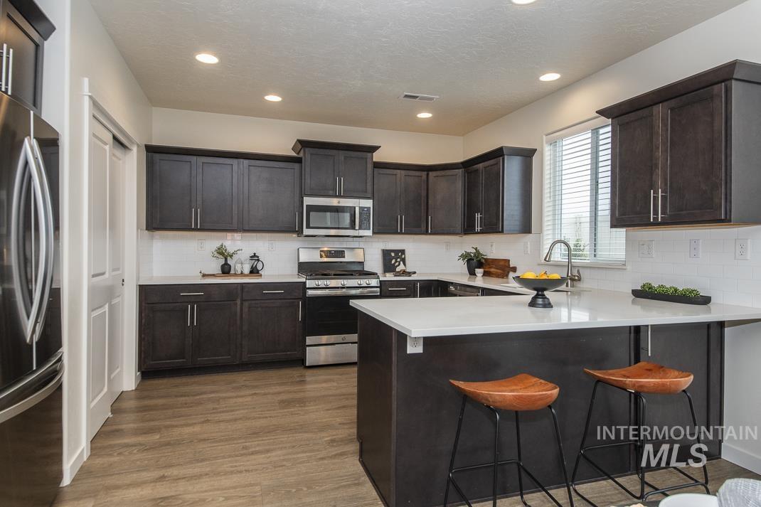 Kitchen with a breakfast bar, a peninsula, stainless steel appliances, decorative backsplash, and recessed lighting