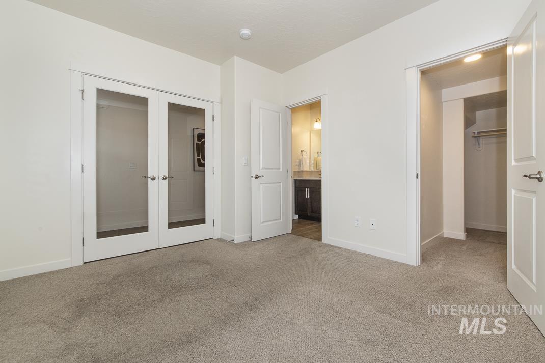 Unfurnished bedroom with french doors, light colored carpet, and ensuite bath