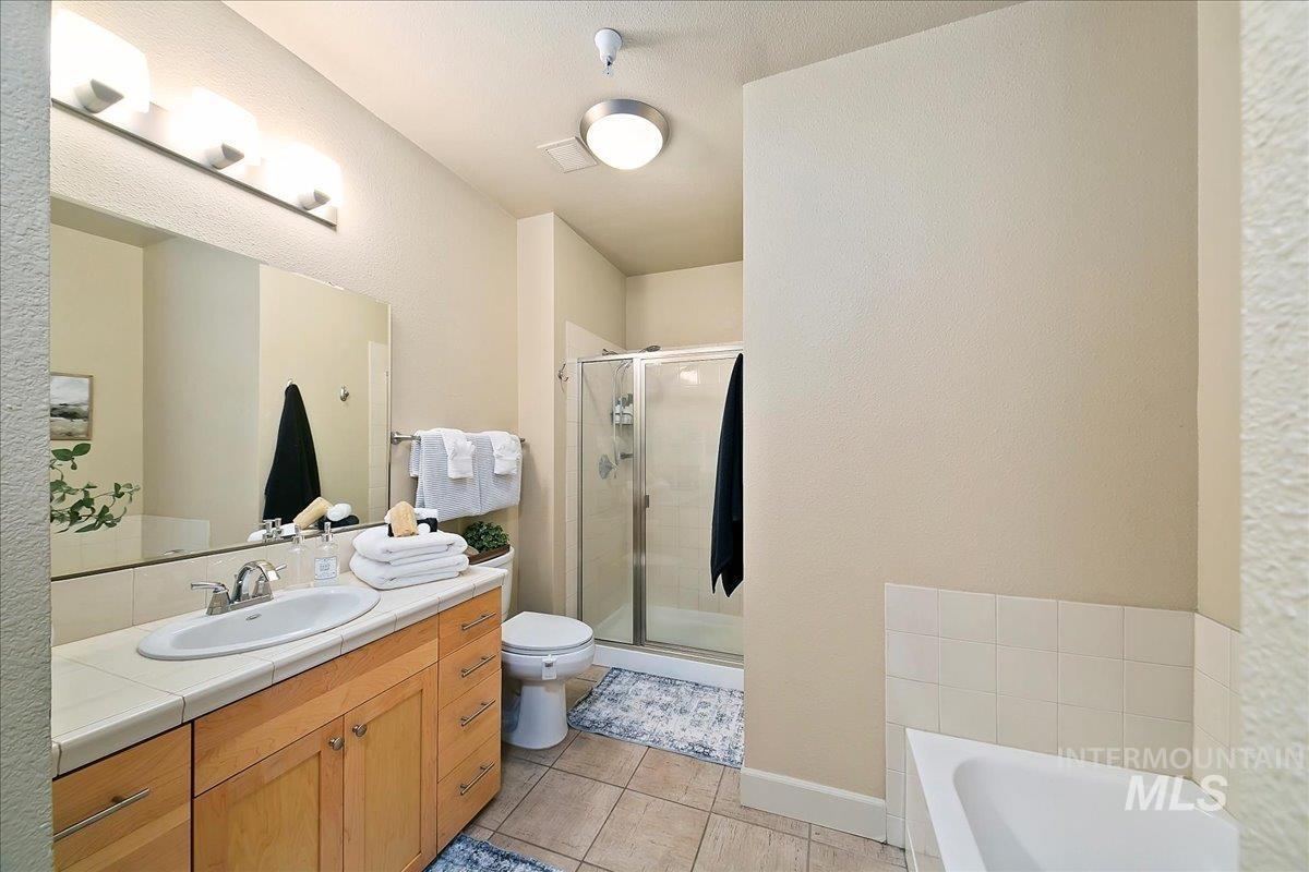 Full bath with a textured wall, vanity, a stall shower, light tile patterned floors, and a garden tub