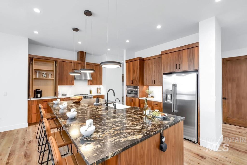 Kitchen with hanging light fixtures, appliances with stainless steel finishes, light wood-style flooring, dark stone counters, and recessed lighting