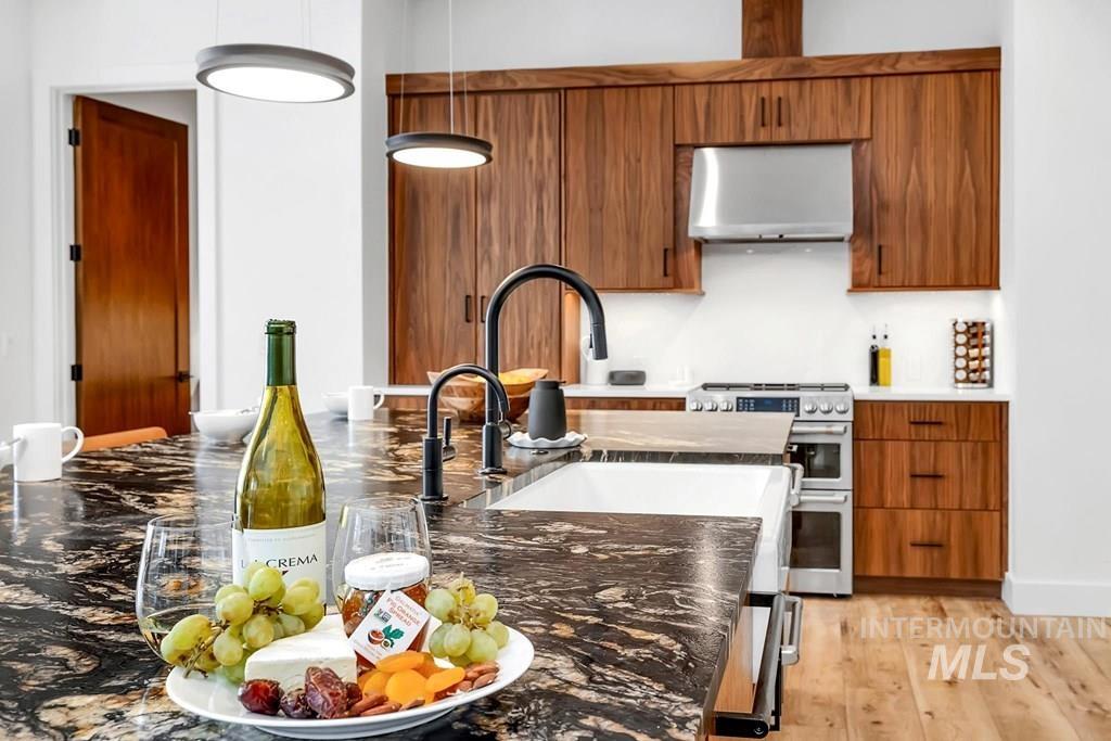 Kitchen featuring brown cabinets, range with two ovens, dark stone counters, and under cabinet range hood