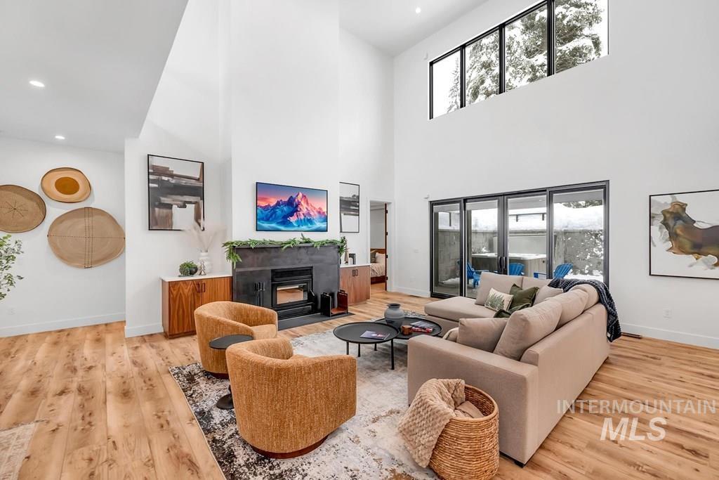 Living area featuring a fireplace with flush hearth, light wood-style floors, a towering ceiling, and recessed lighting