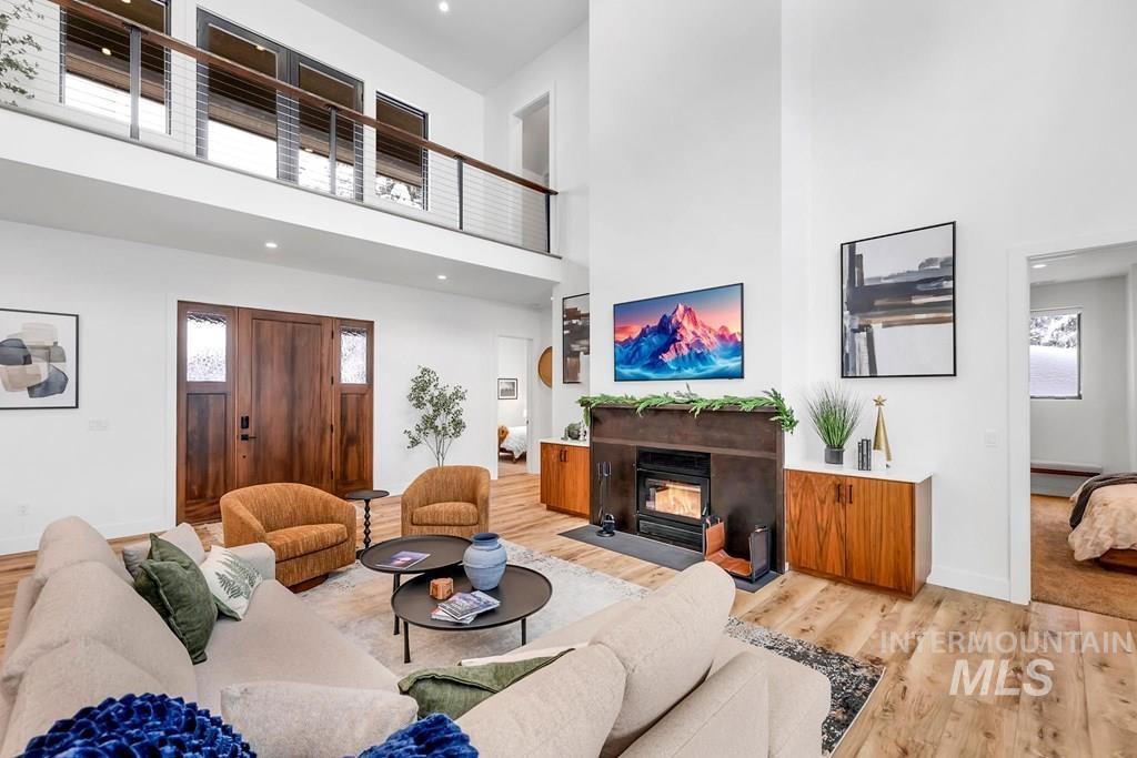 Living room featuring light wood-style flooring, a towering ceiling, a fireplace with flush hearth, and recessed lighting