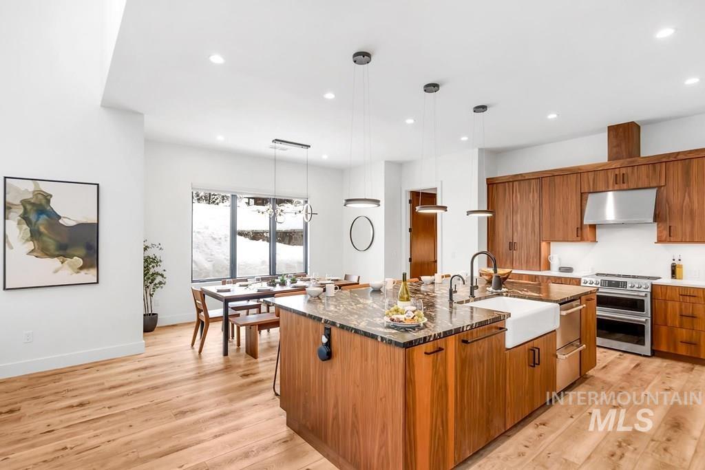 Kitchen with dark stone counters, brown cabinets, a large island, hanging light fixtures, and recessed lighting
