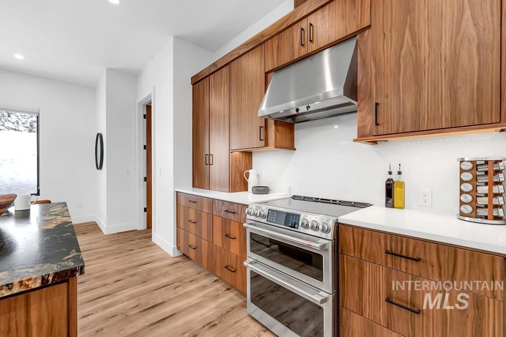 Kitchen with range with two ovens, brown cabinetry, under cabinet range hood, light wood-type flooring, and recessed lighting