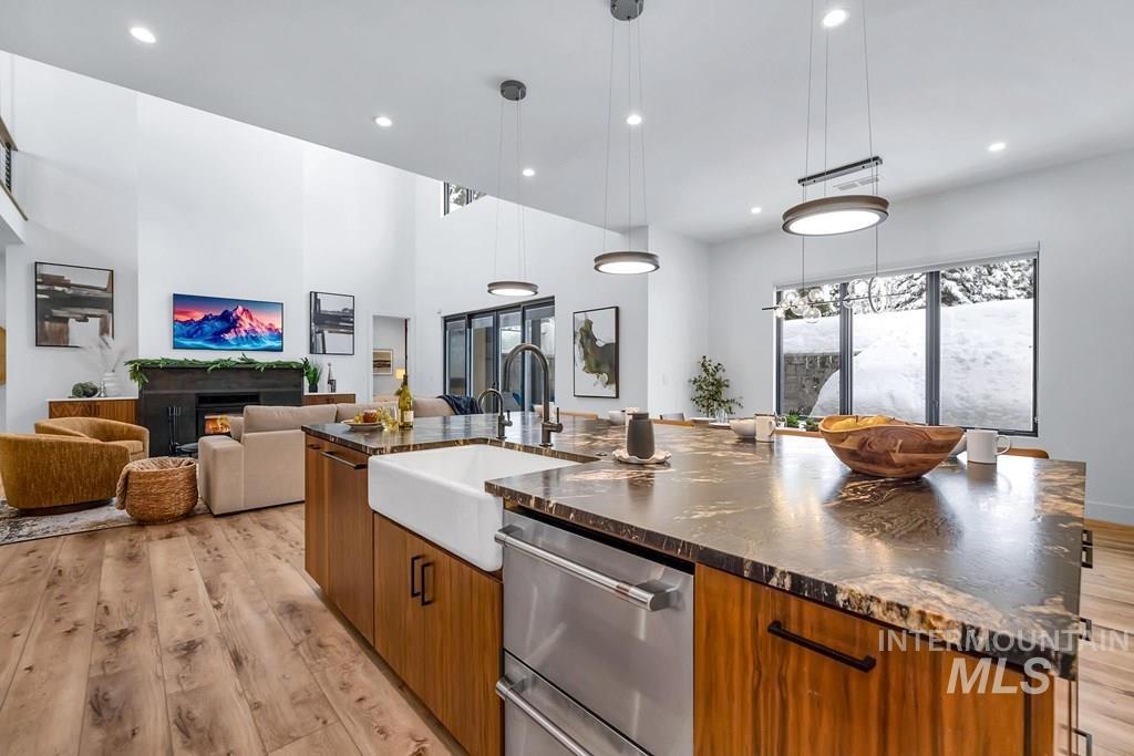 Kitchen featuring brown cabinets, a spacious island, stainless steel dishwasher, open floor plan, and light wood-style flooring