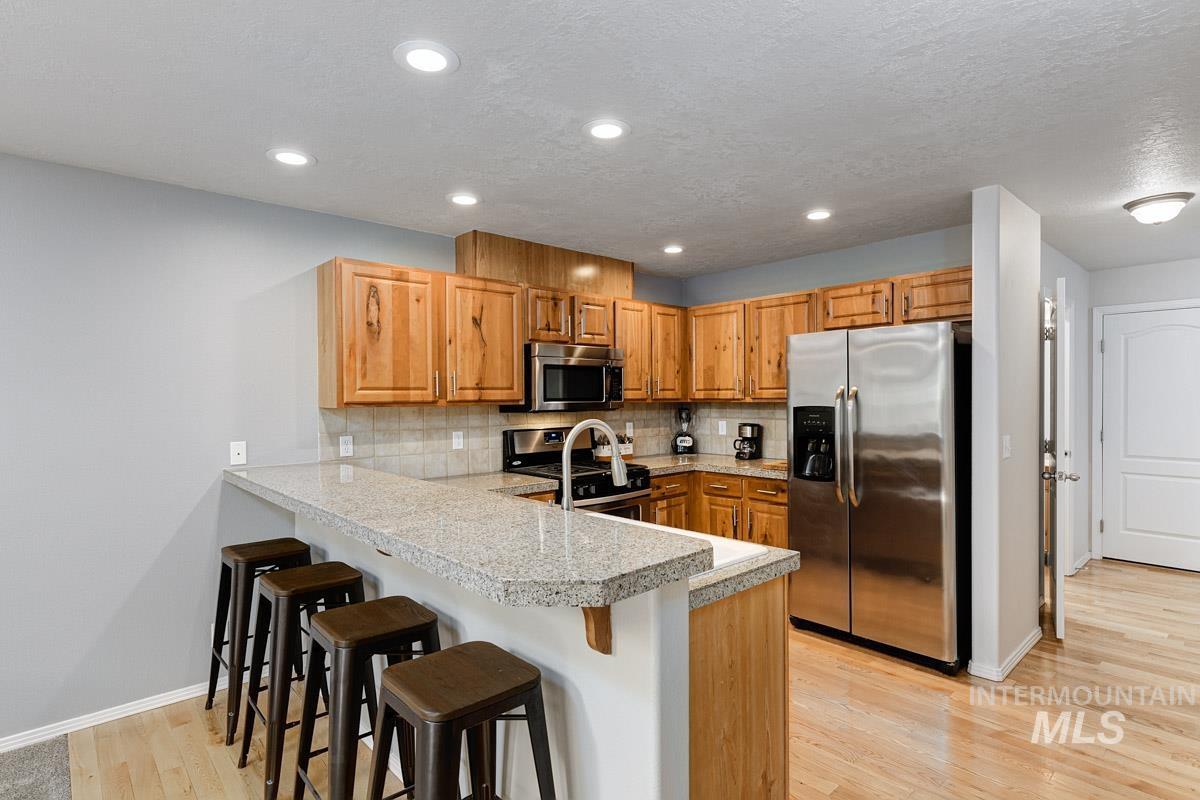 Kitchen with stainless steel appliances, a peninsula, a kitchen breakfast bar, backsplash, and light wood-style flooring