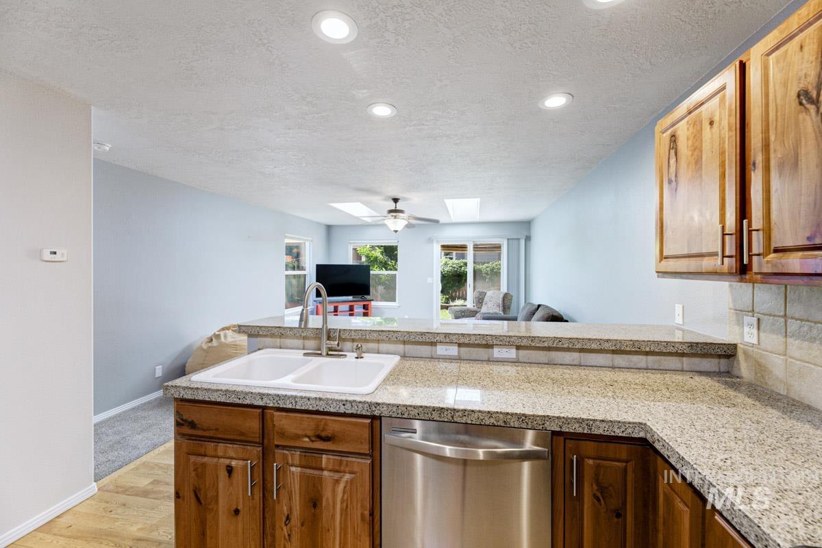 Kitchen featuring a skylight, stainless steel dishwasher, a textured ceiling, light wood finished floors, and light countertops
