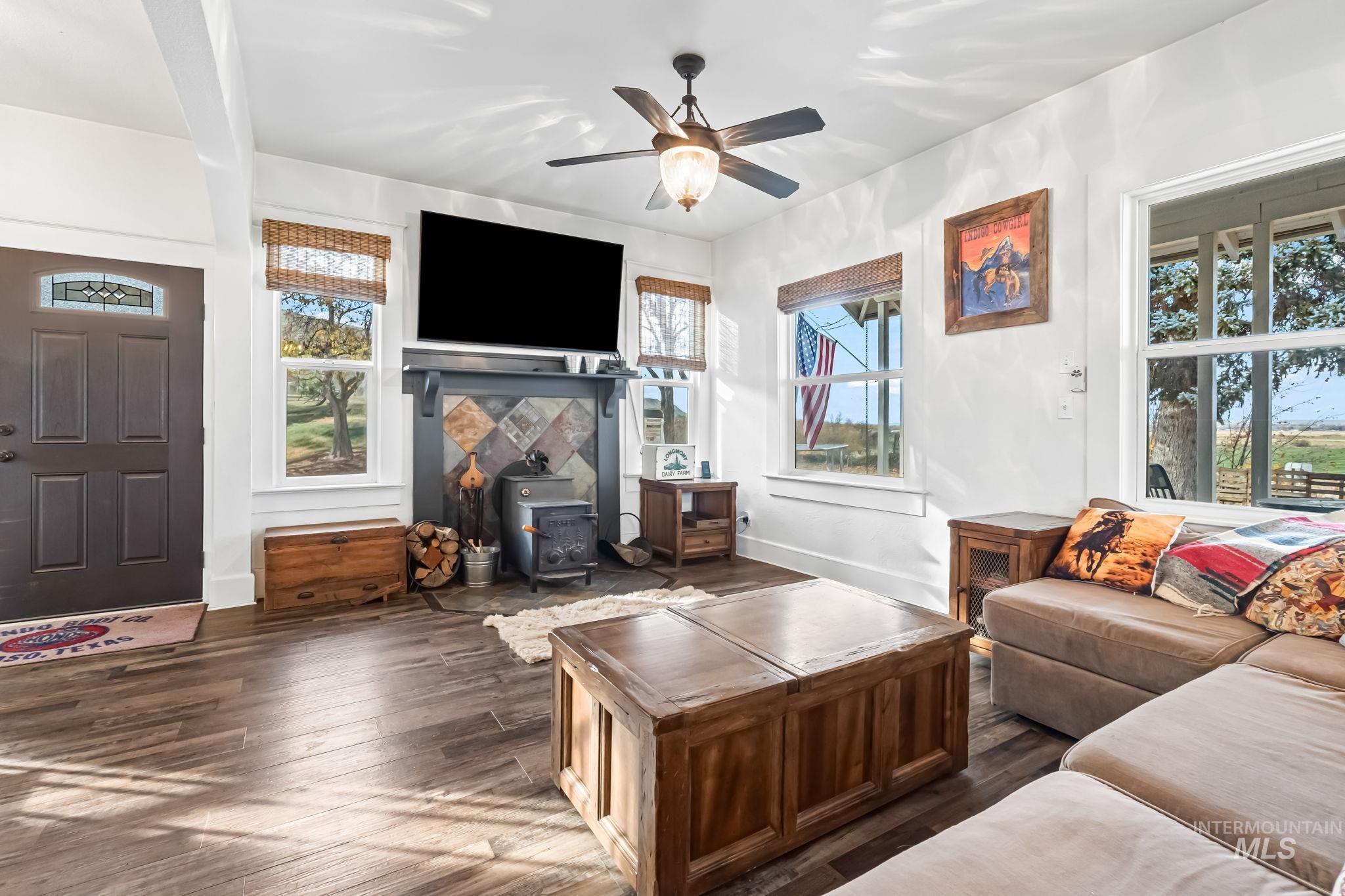 Living room with dark wood finished floors, a wood stove, healthy amount of natural light, and a ceiling fan