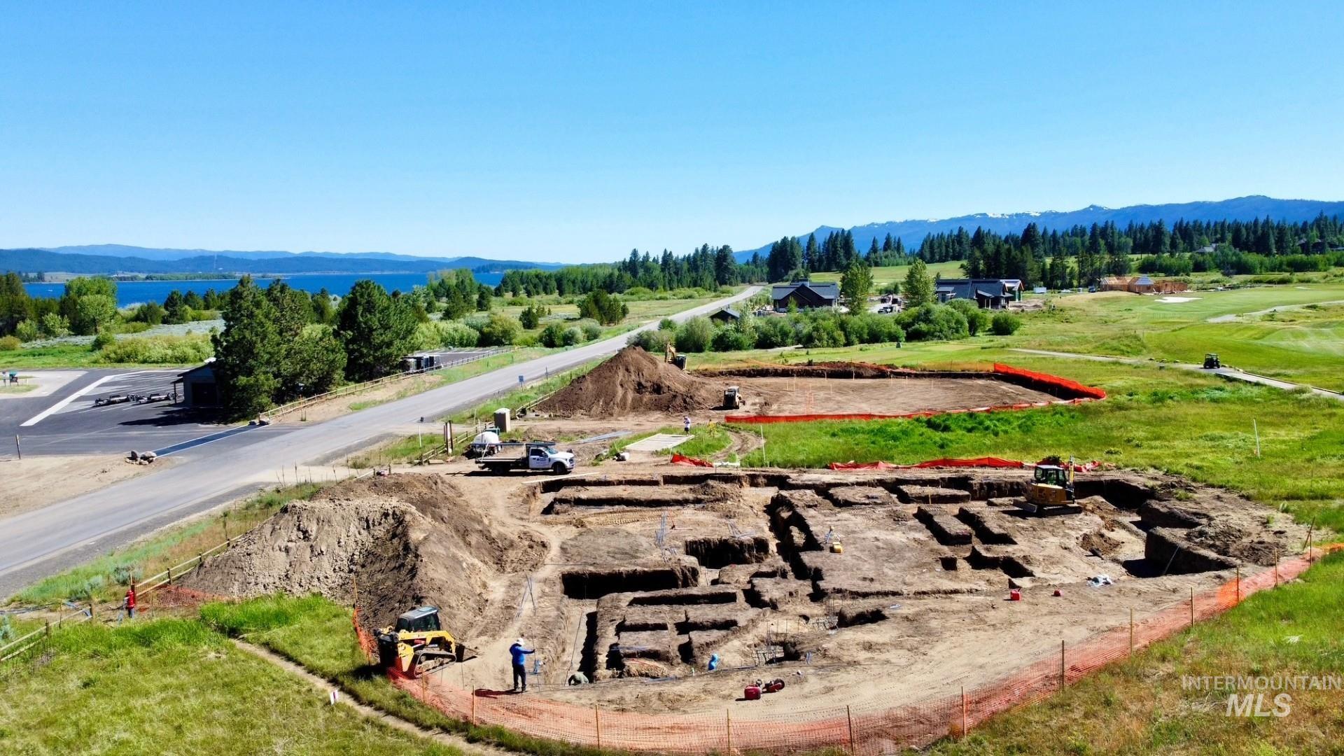 Expansive building lot featuring excavated foundations, mature green landscaping, and distant mountain ranges