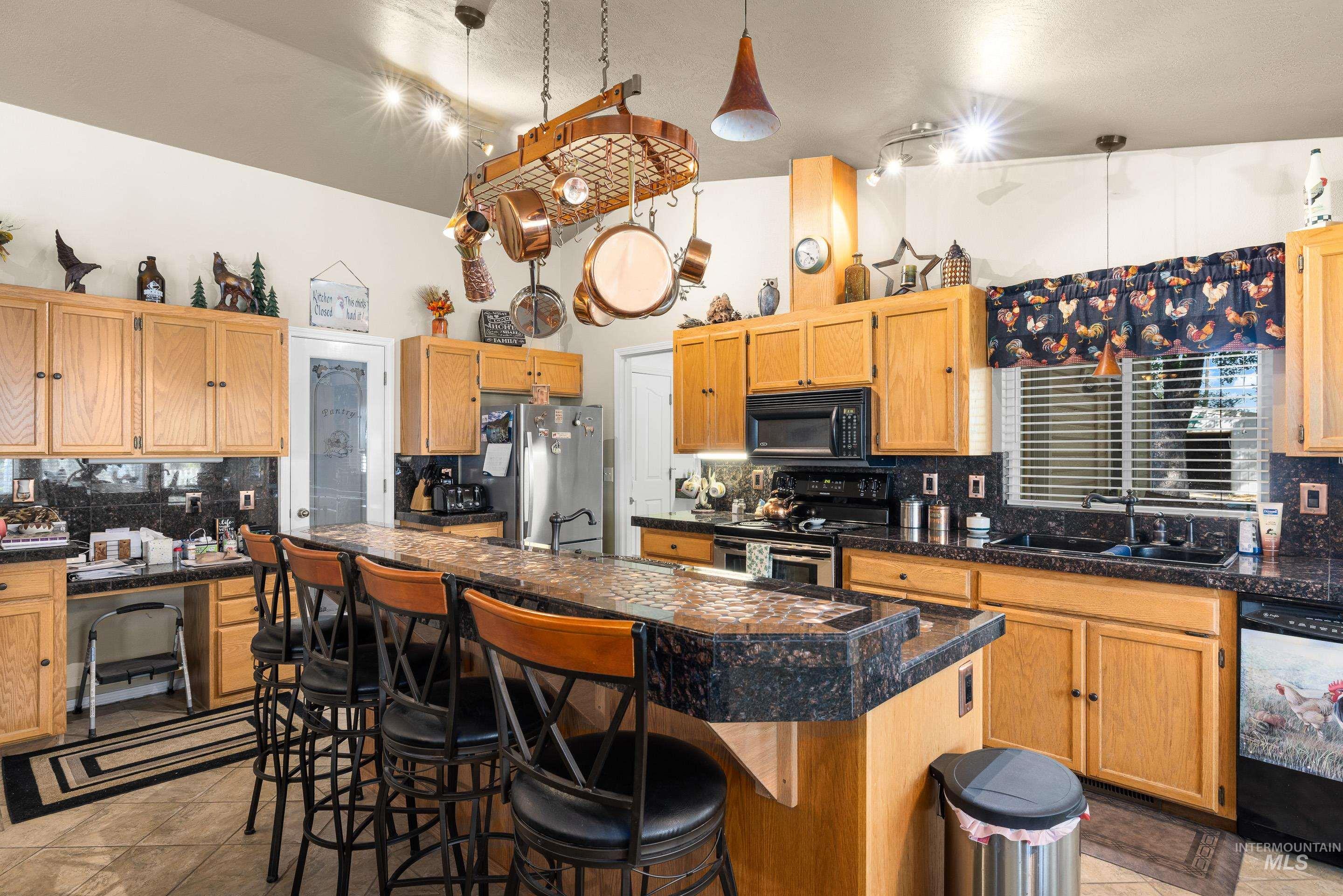 Kitchen featuring decorative backsplash, black appliances, a kitchen breakfast bar, tile counters, and light tile patterned floors