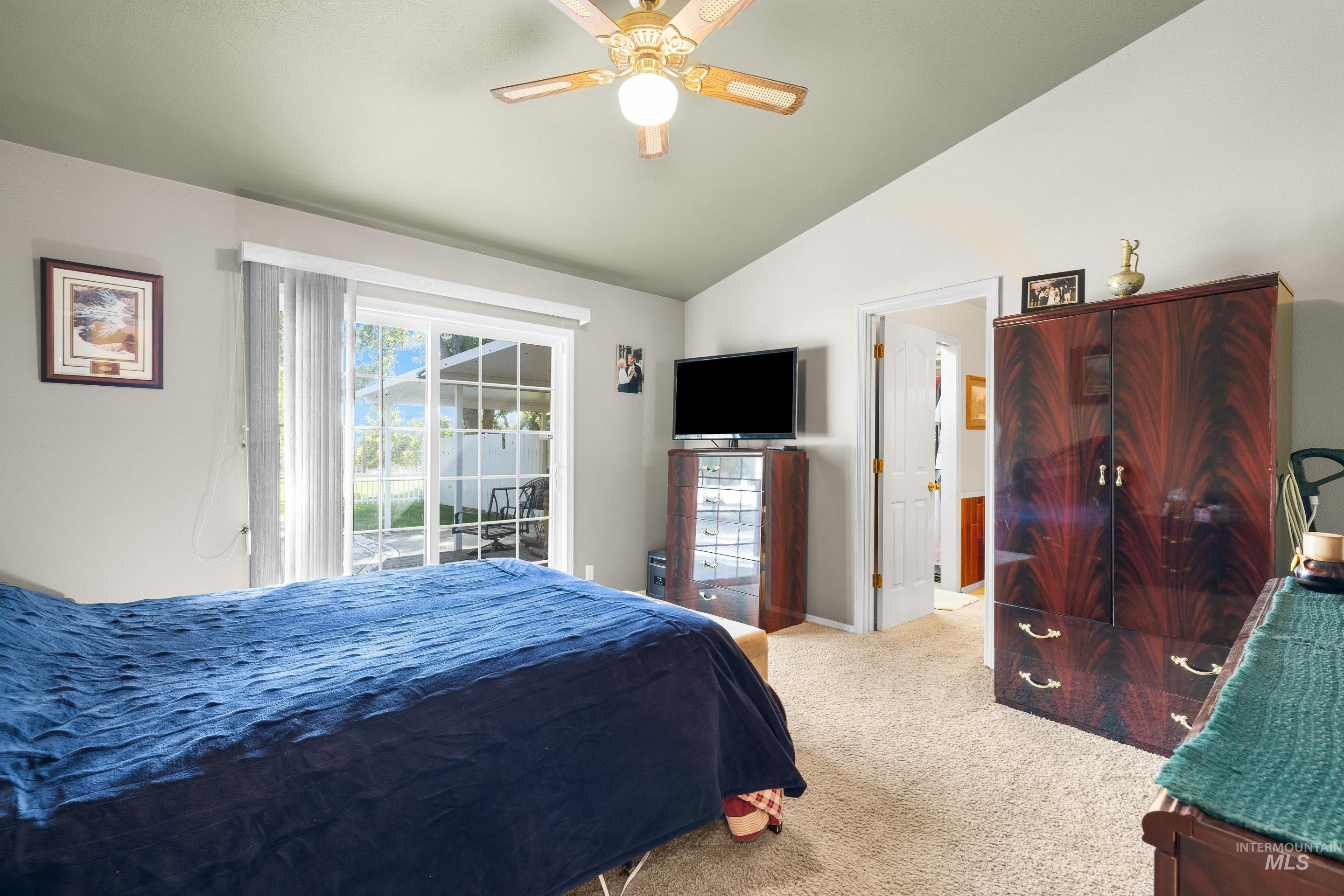 Carpeted bedroom featuring access to outside, vaulted ceiling, and ceiling fan