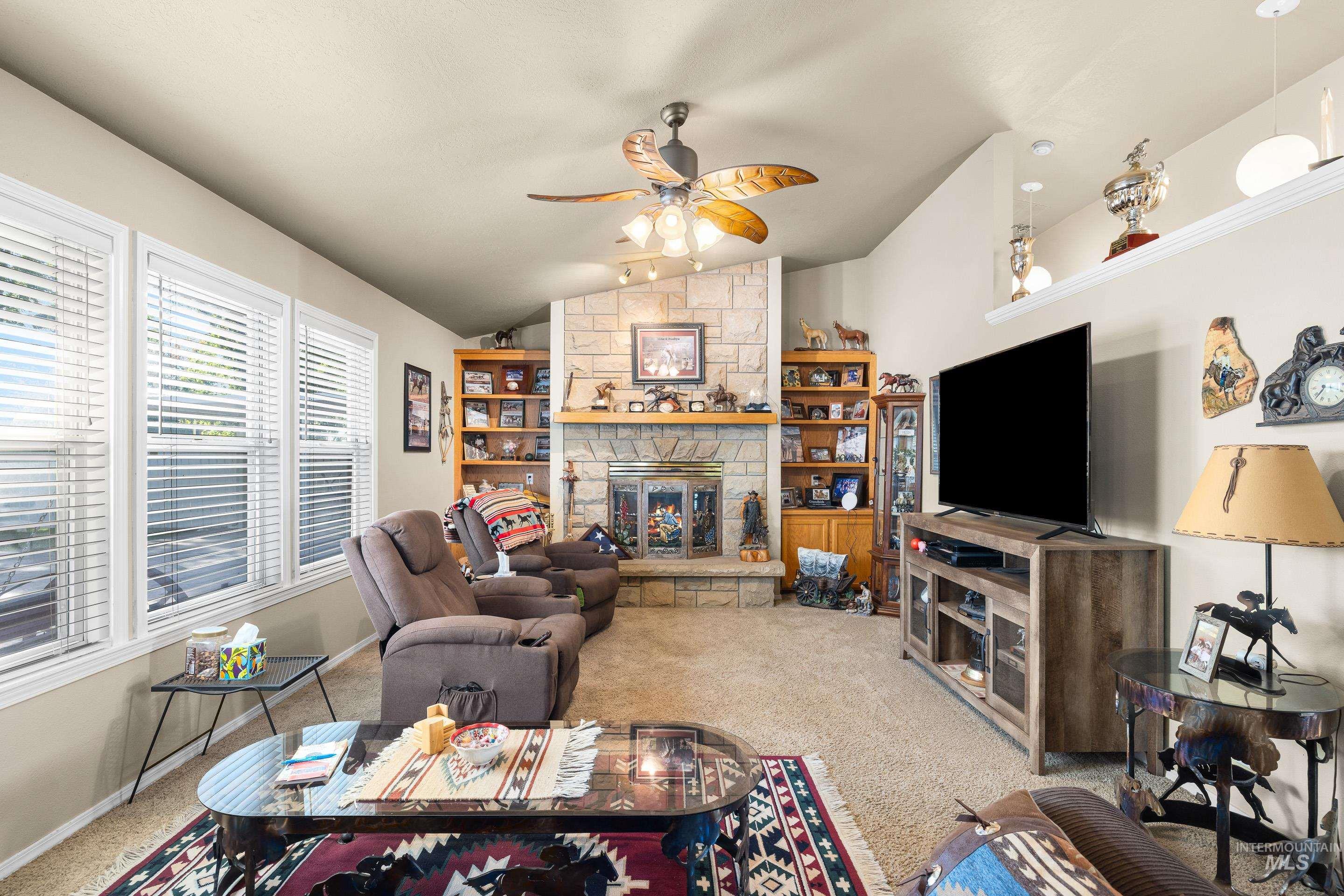 Living area featuring carpet floors, vaulted ceiling, ceiling fan, and a stone fireplace