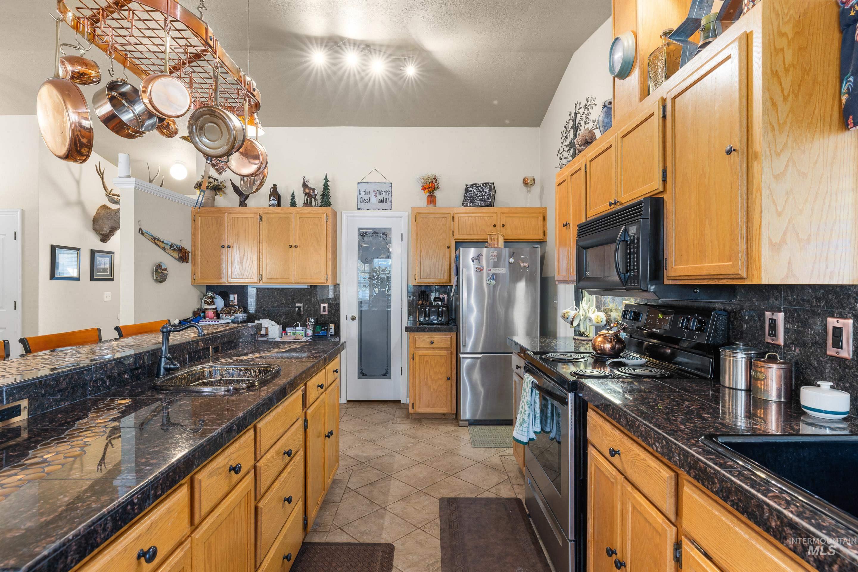 Kitchen featuring black appliances, decorative backsplash, a kitchen bar, light tile patterned floors, and tile countertops