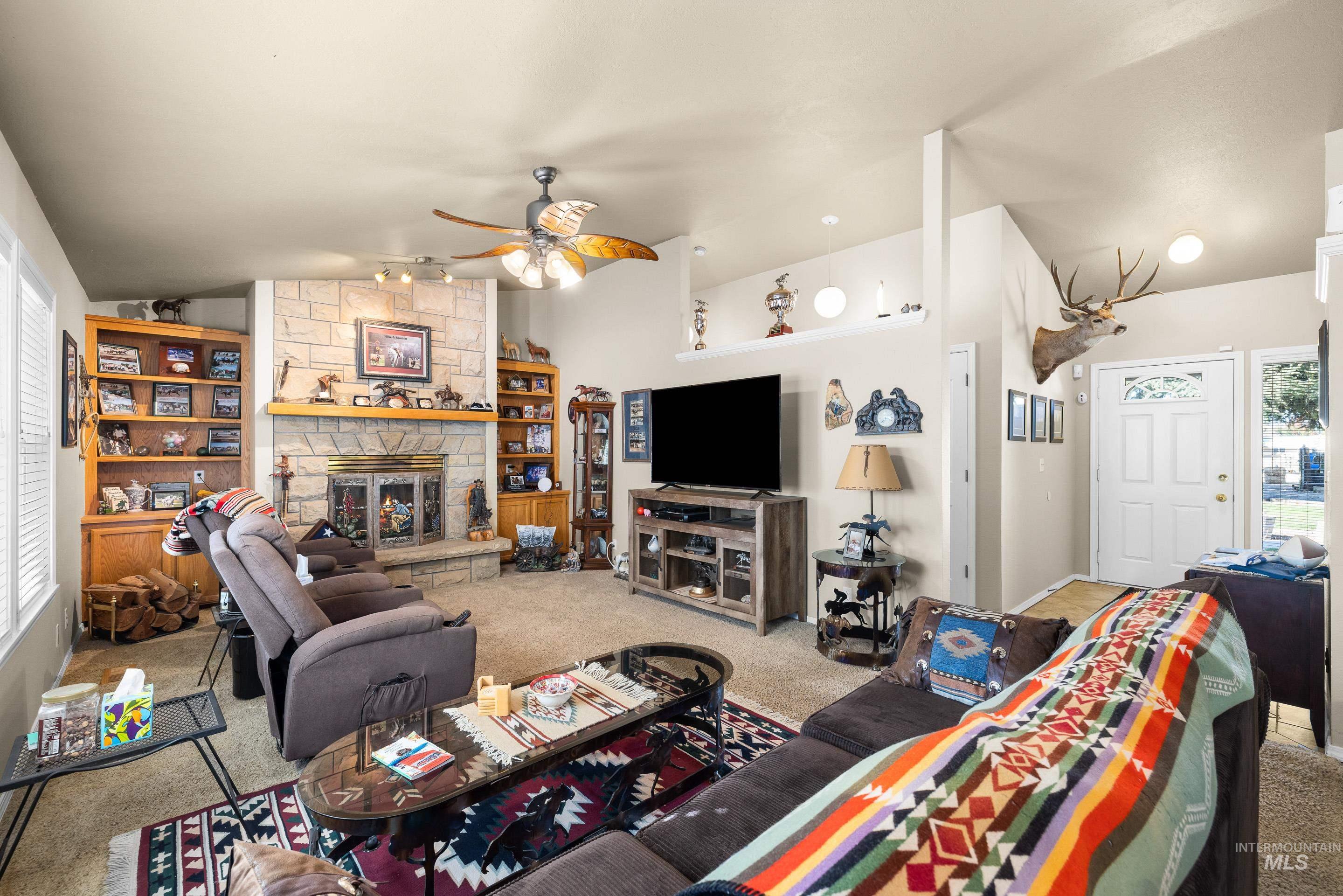 Living area featuring lofted ceiling, carpet flooring, a fireplace, and a ceiling fan