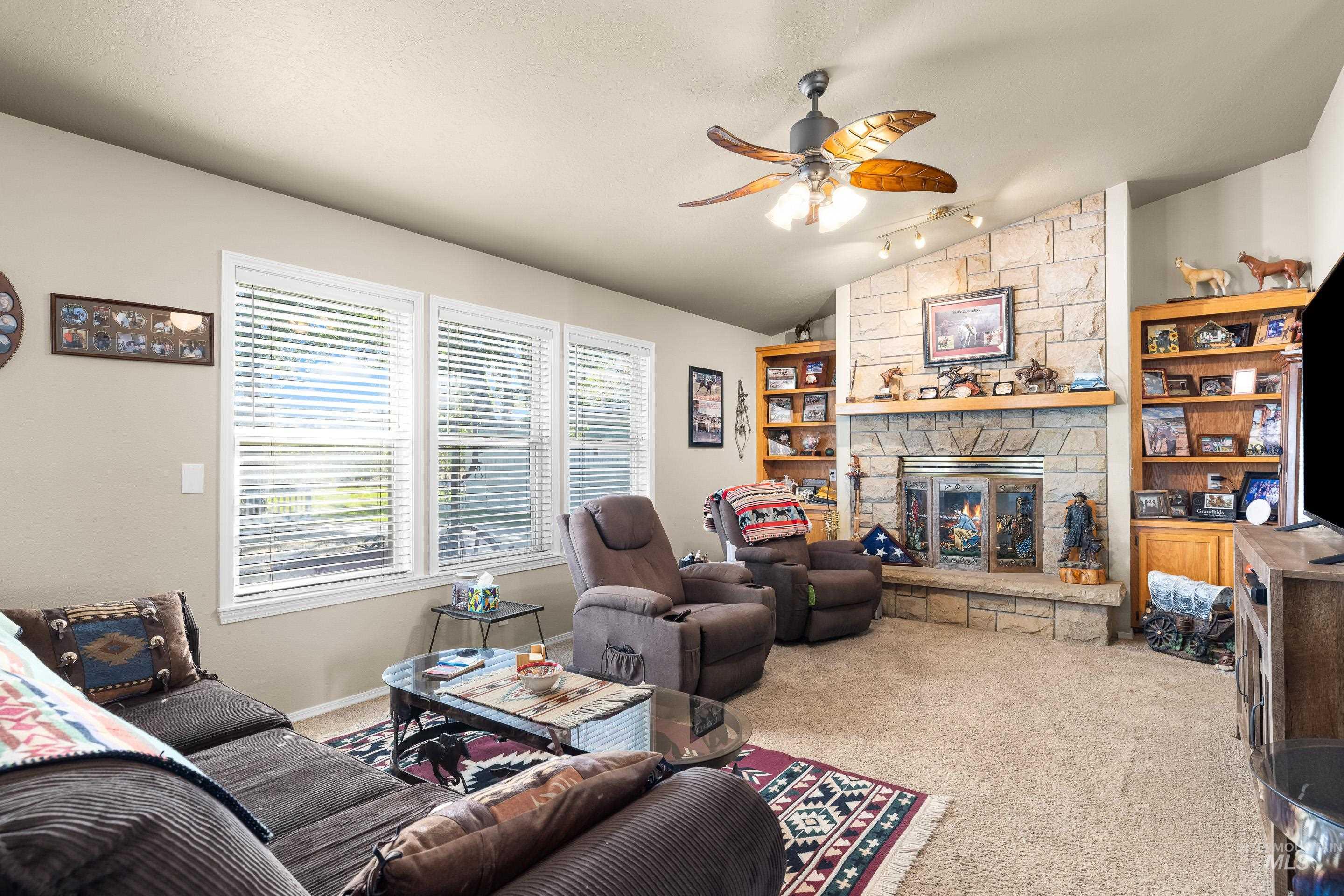 Carpeted living room featuring vaulted ceiling, a fireplace, ceiling fan, and rail lighting