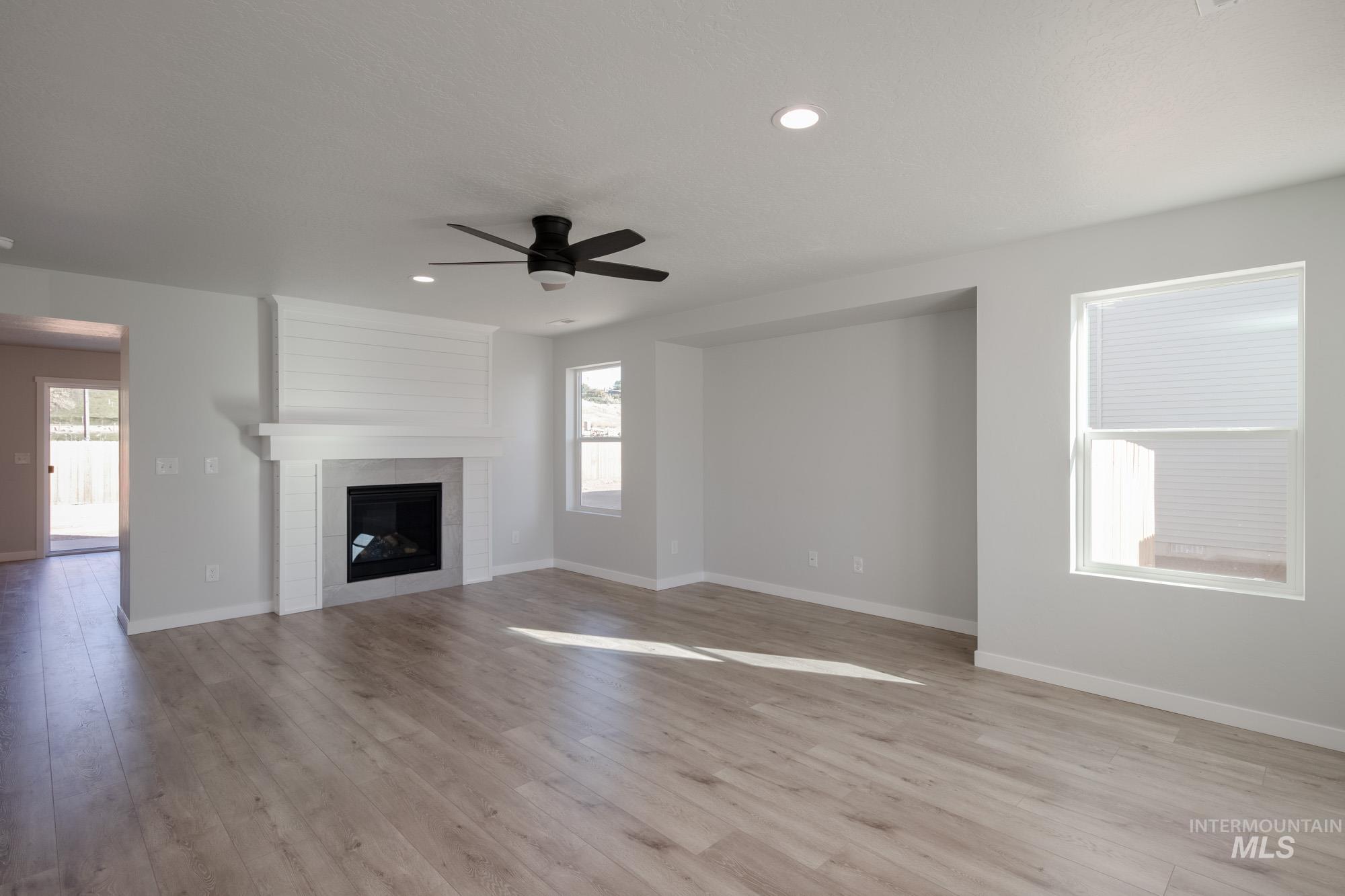 Unfurnished living room featuring a tiled fireplace, light wood-style flooring, a ceiling fan, and recessed lighting