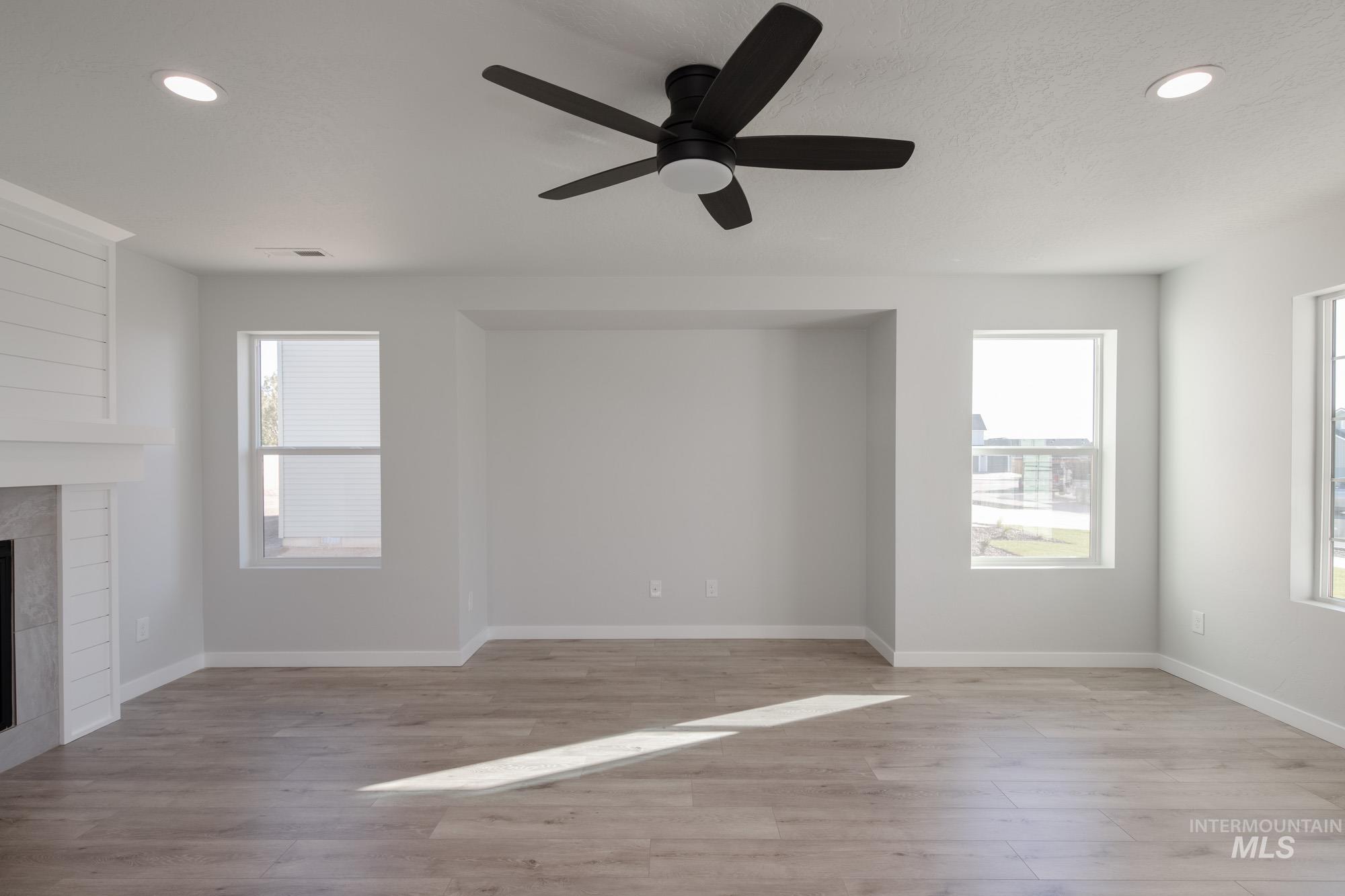 Unfurnished living room featuring recessed lighting, plenty of natural light, light wood-type flooring, a large fireplace, and ceiling fan