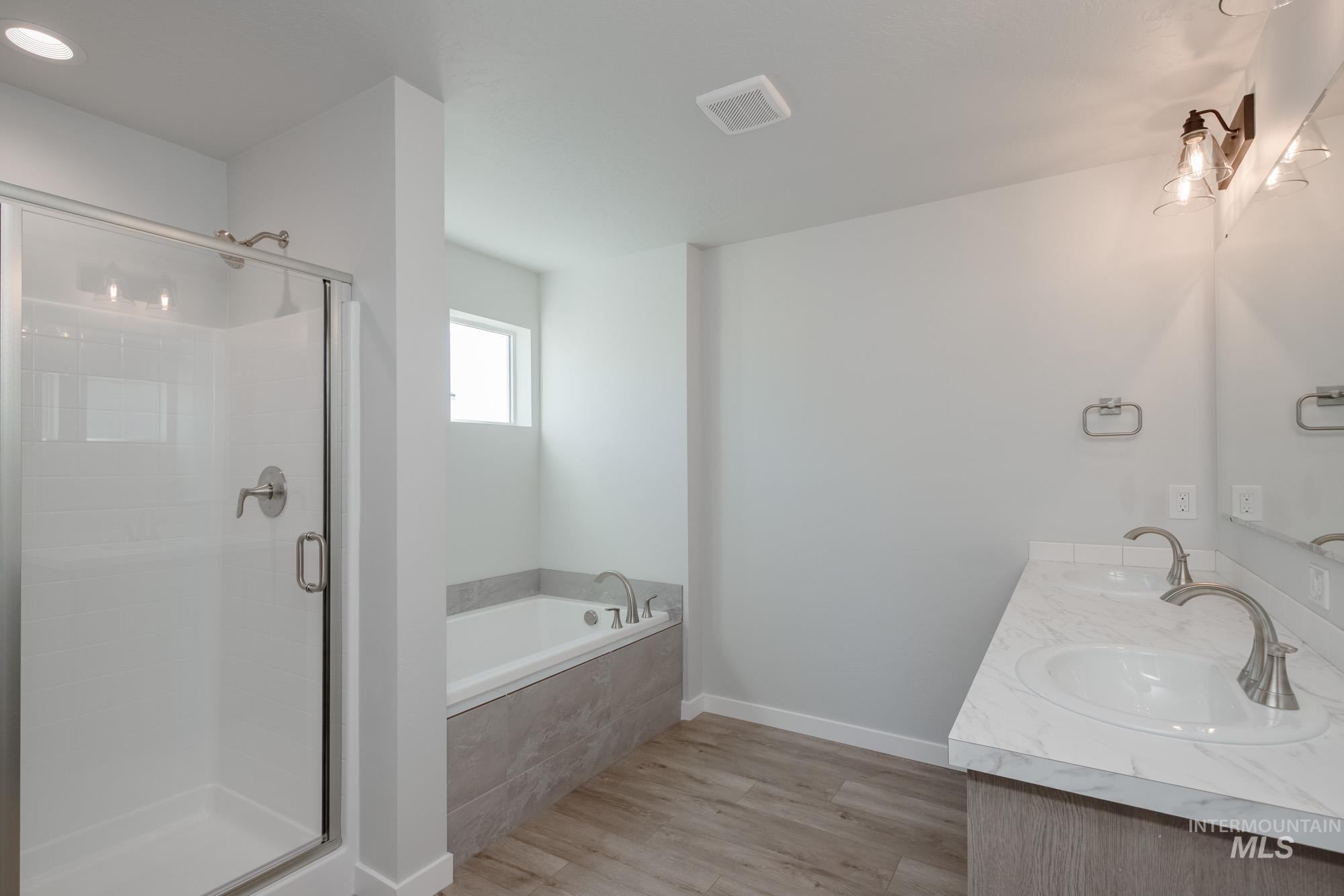 Full bath featuring light wood-style flooring, double vanity, a shower stall, and a garden tub