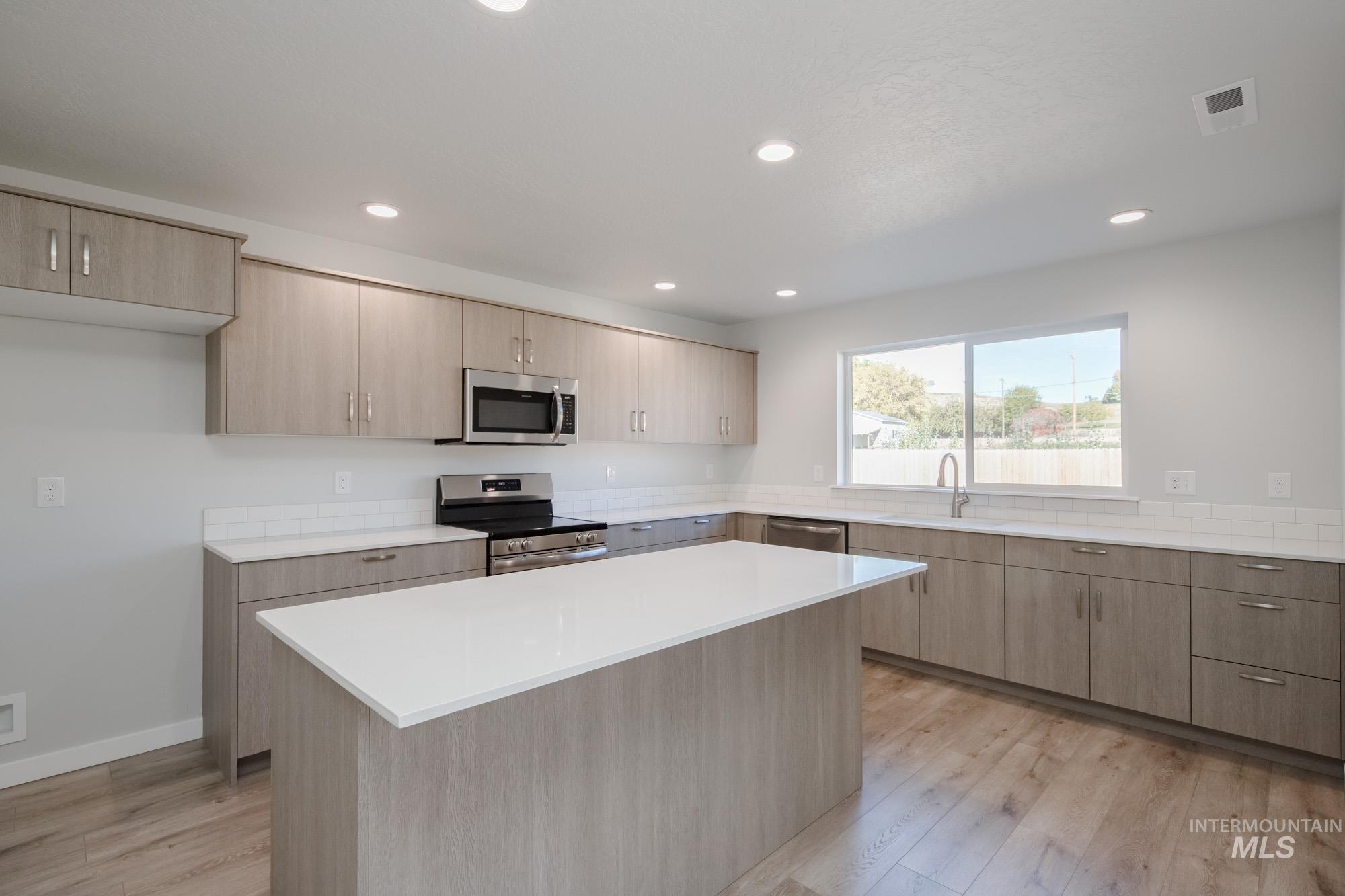 Kitchen featuring light brown cabinetry, appliances with stainless steel finishes, modern cabinets, light wood-style flooring, and recessed lighting
