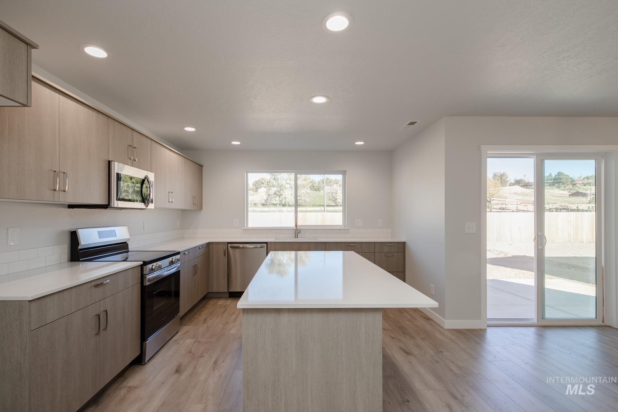 Kitchen featuring appliances with stainless steel finishes, light brown cabinets, recessed lighting, light wood-style floors, and a center island