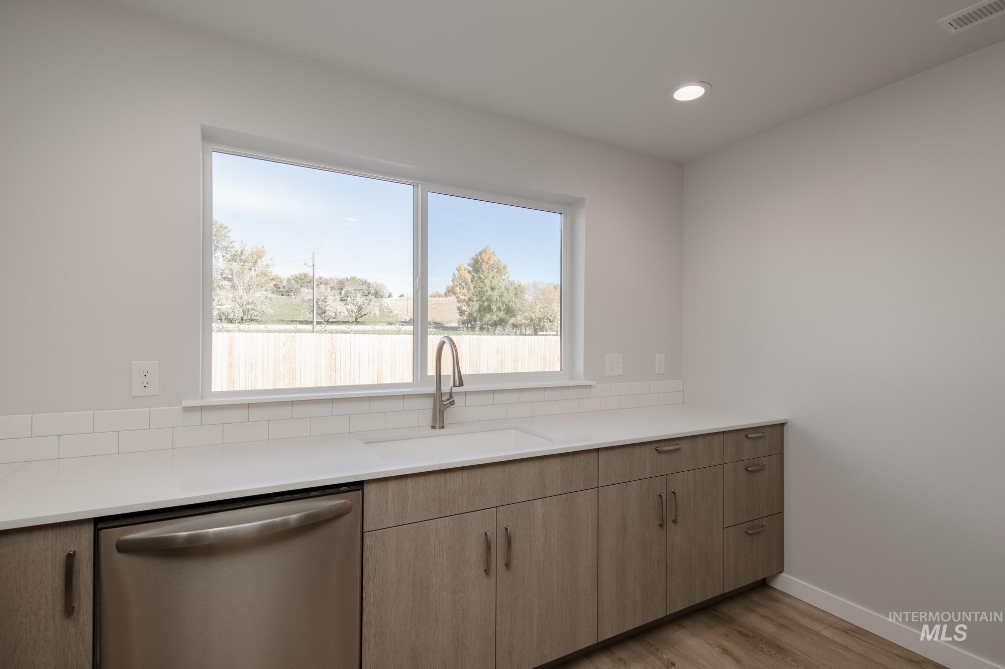Kitchen with stainless steel dishwasher, light wood-style floors, recessed lighting, light stone counters, and light brown cabinets