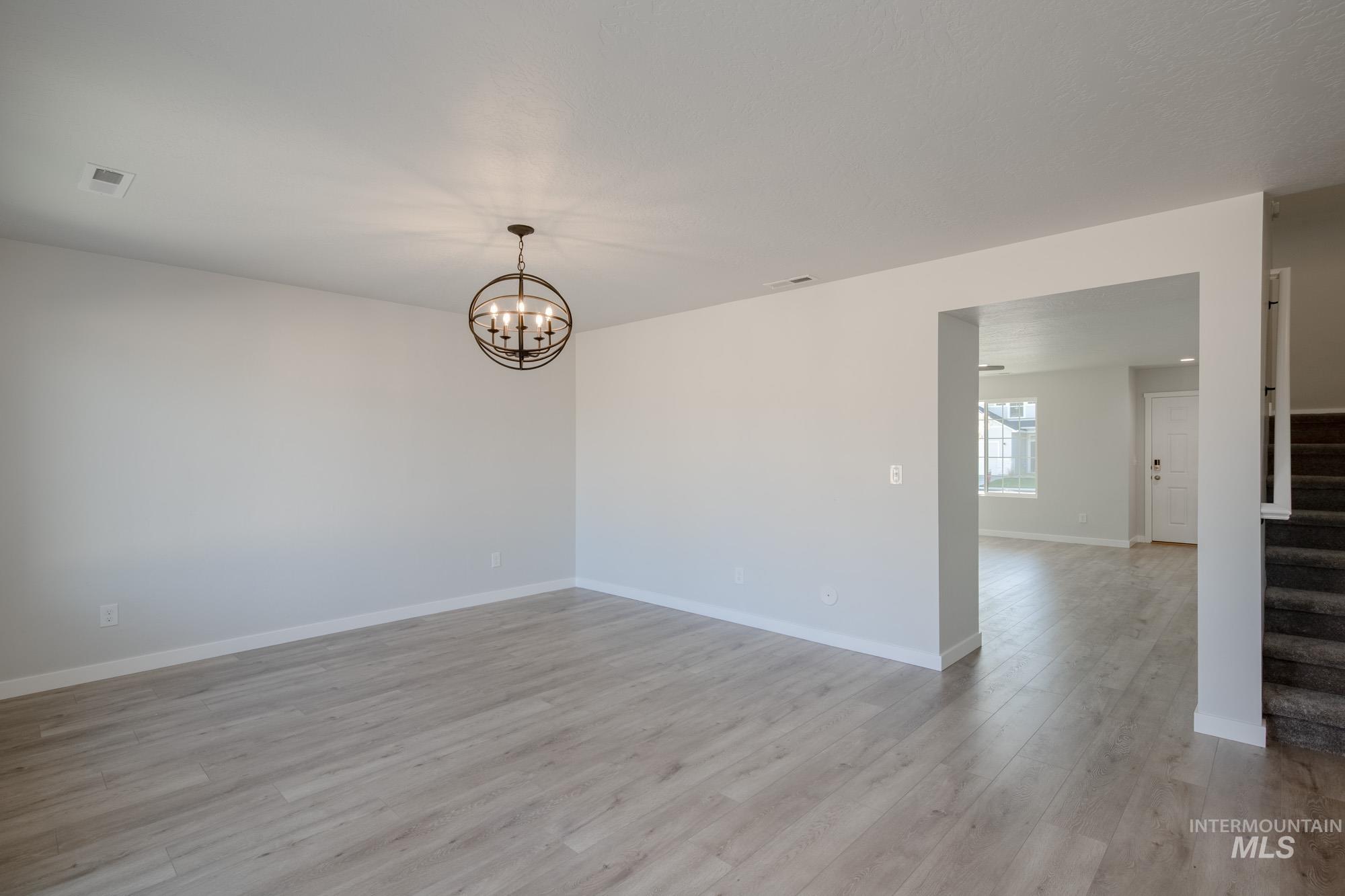 Spare room with light wood-style floors, stairs, and a chandelier