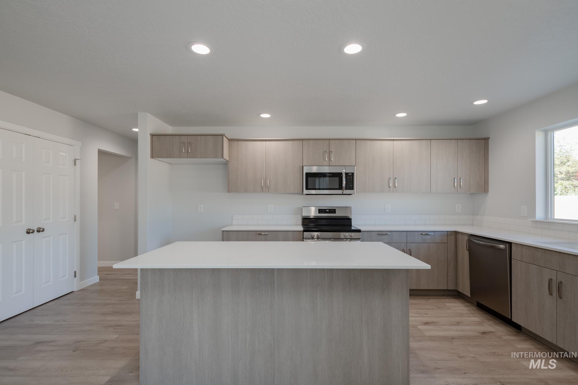 Kitchen with stainless steel appliances, a kitchen island, light brown cabinets, light wood-type flooring, and modern cabinets