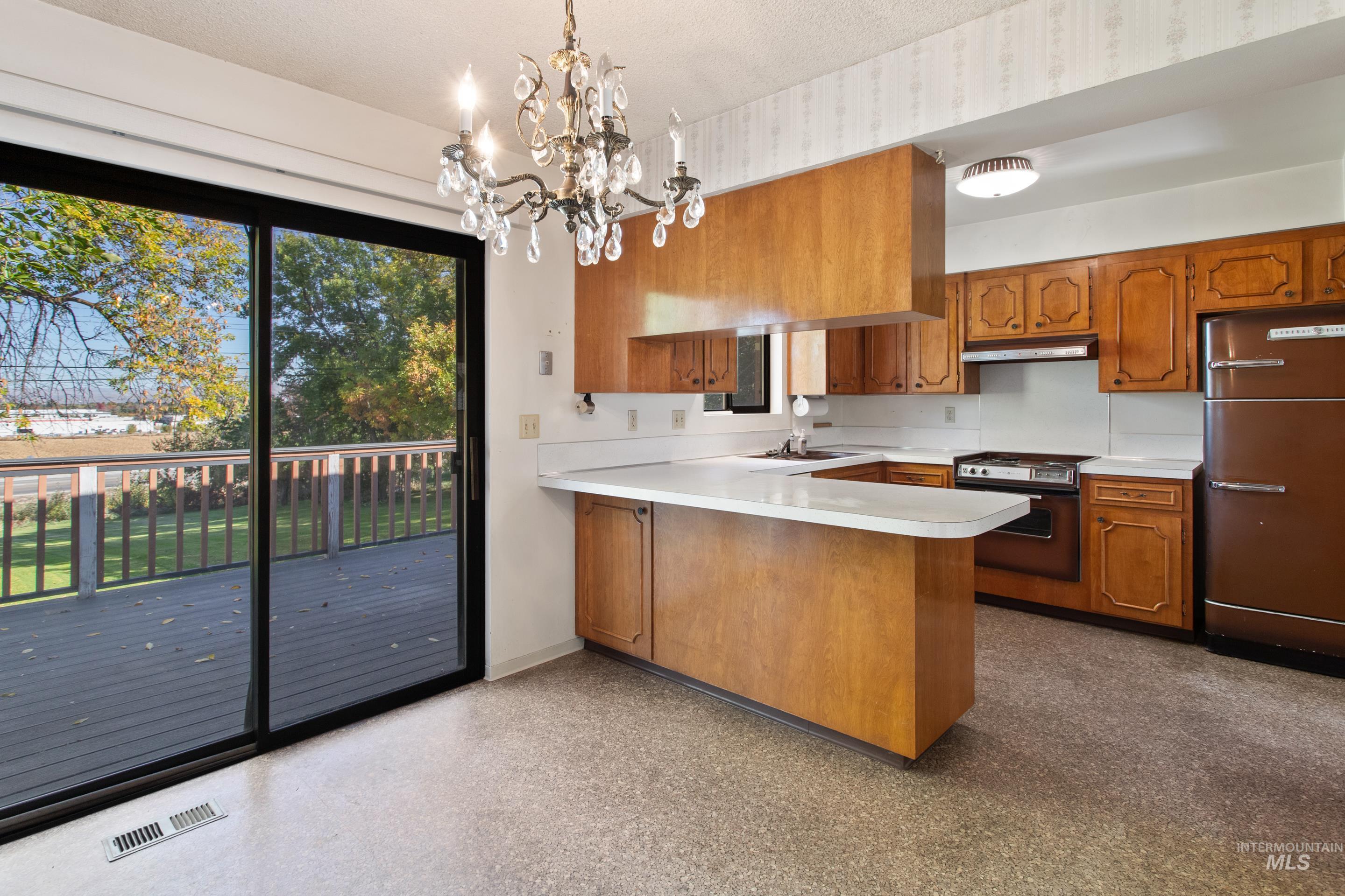 Kitchen with brown cabinets, plenty of natural light, a peninsula, light countertops, and a textured ceiling