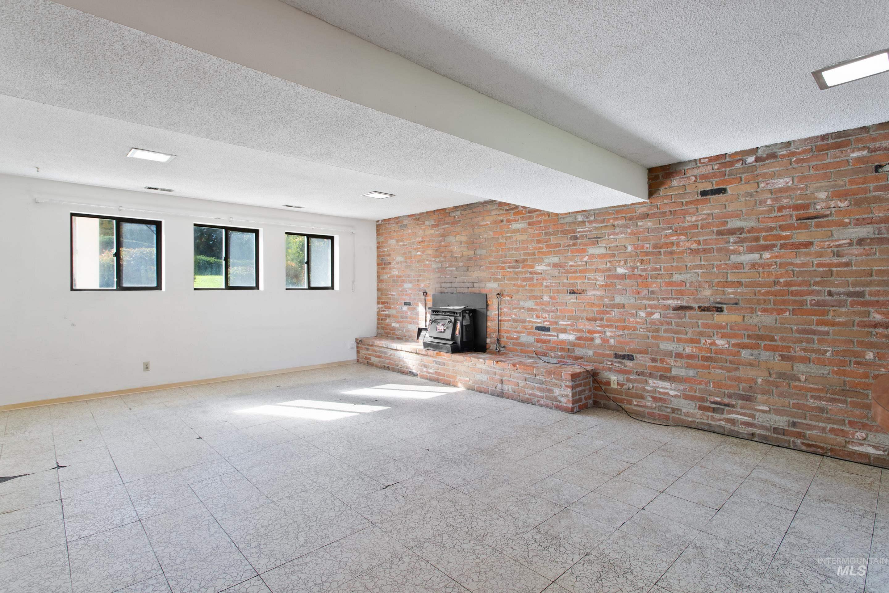Unfurnished living room featuring a wood stove, brick wall, a textured ceiling, and tile patterned floors