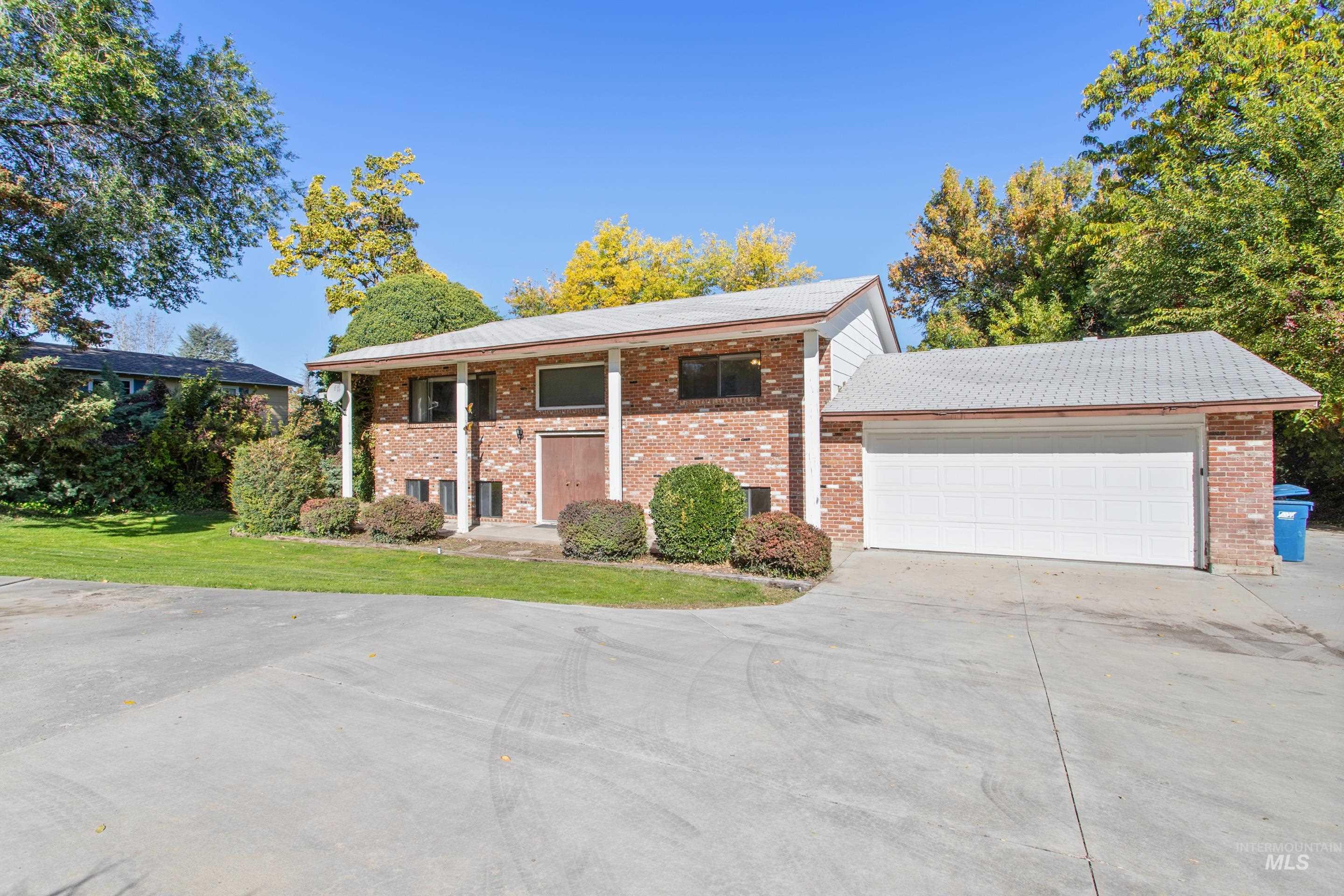 View of front of house with a front yard, driveway, brick siding, an attached garage, and covered porch