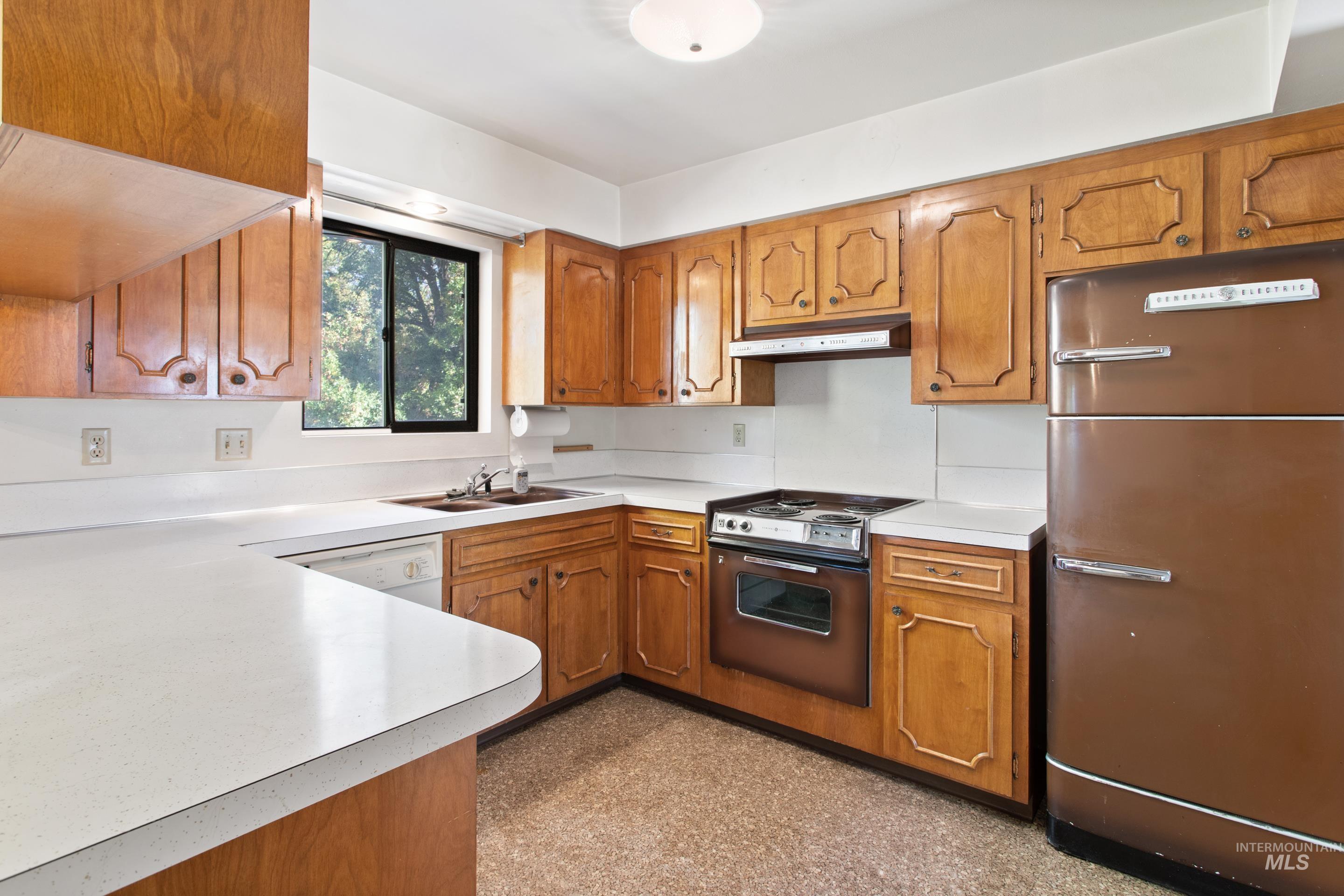 Kitchen with brown cabinets, freestanding refrigerator, light countertops, and electric range oven