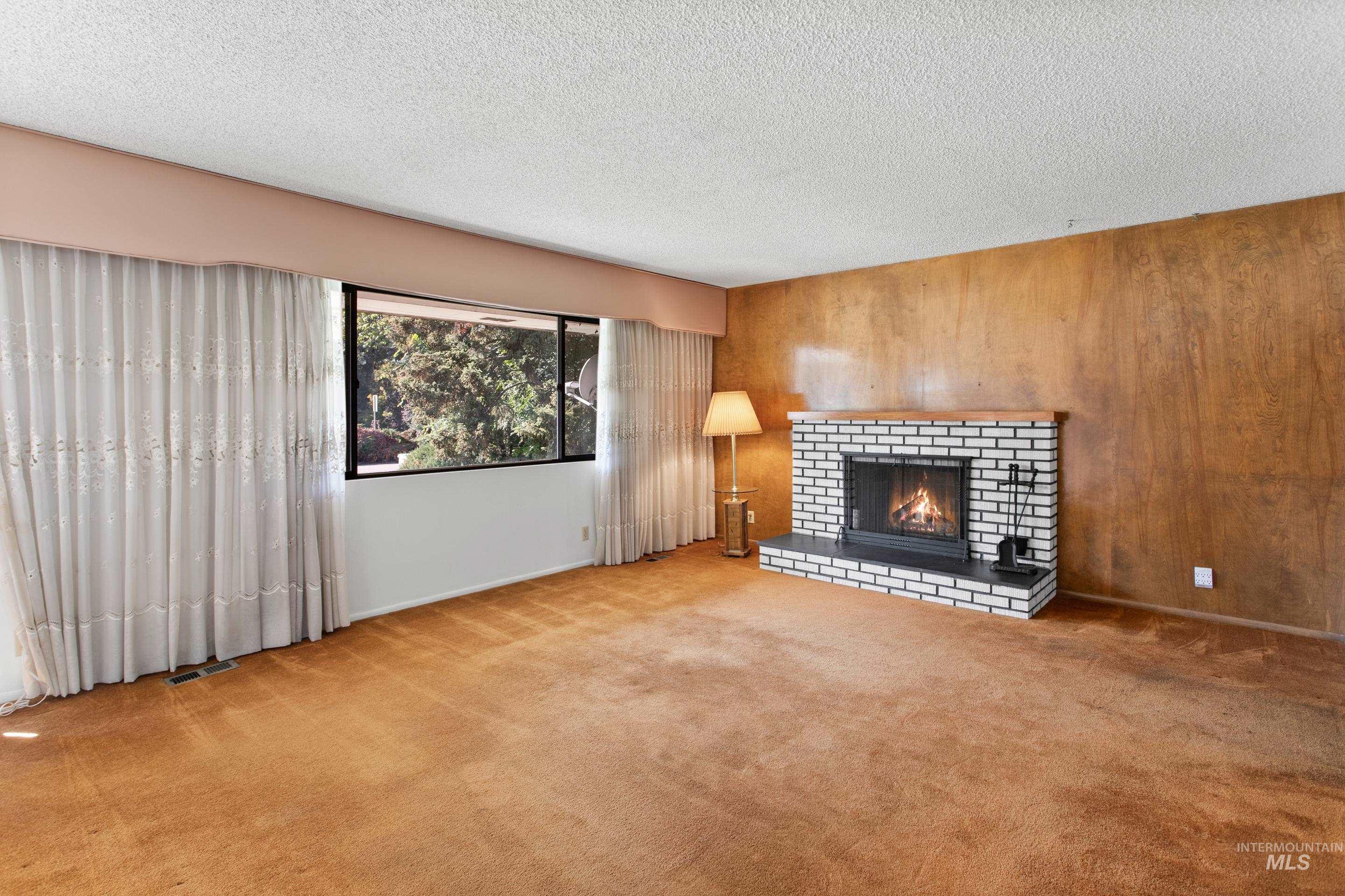 Unfurnished living room with carpet, a fireplace, wood walls, and a textured ceiling