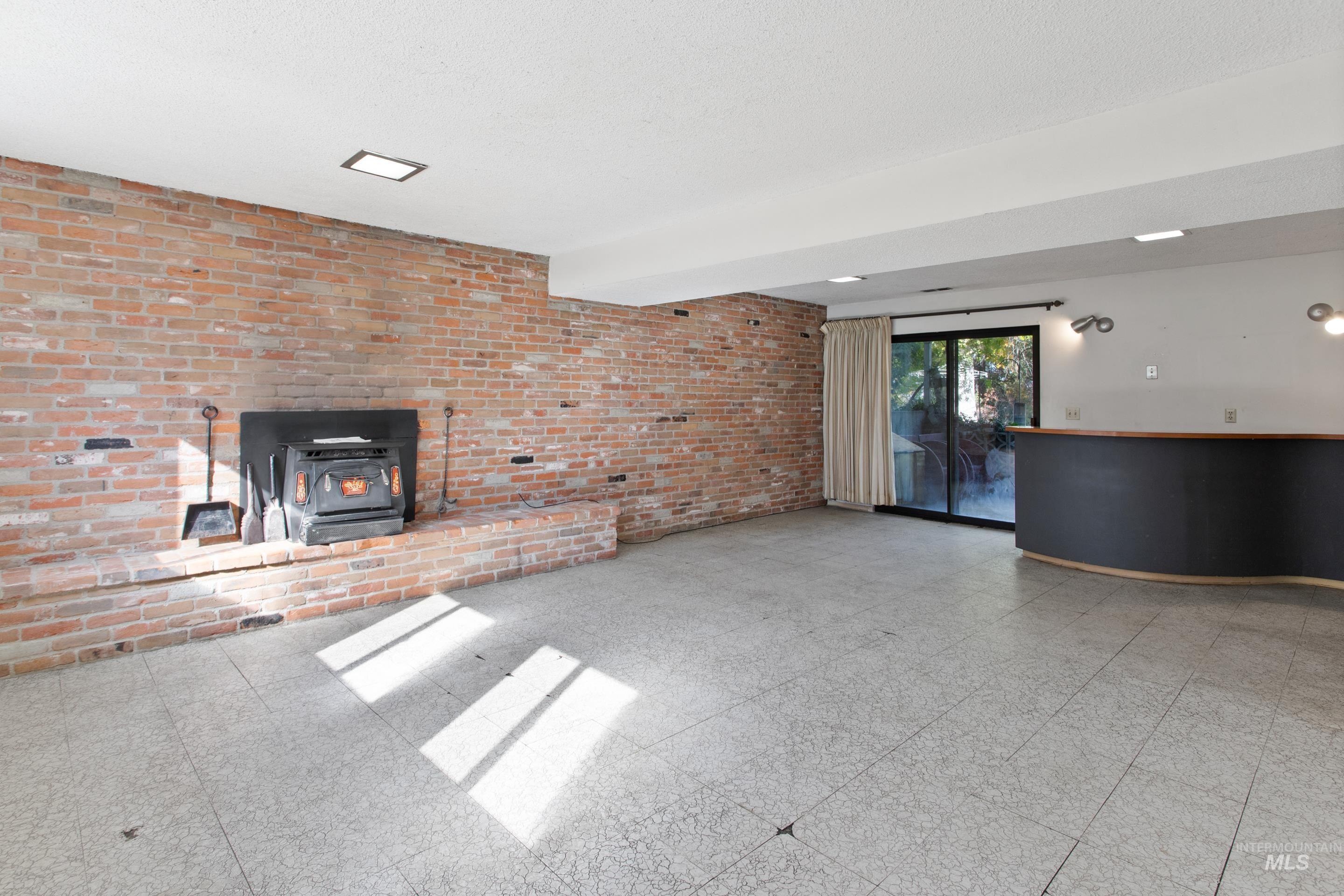 Unfurnished living room featuring brick wall, a wood stove, and tile patterned floors