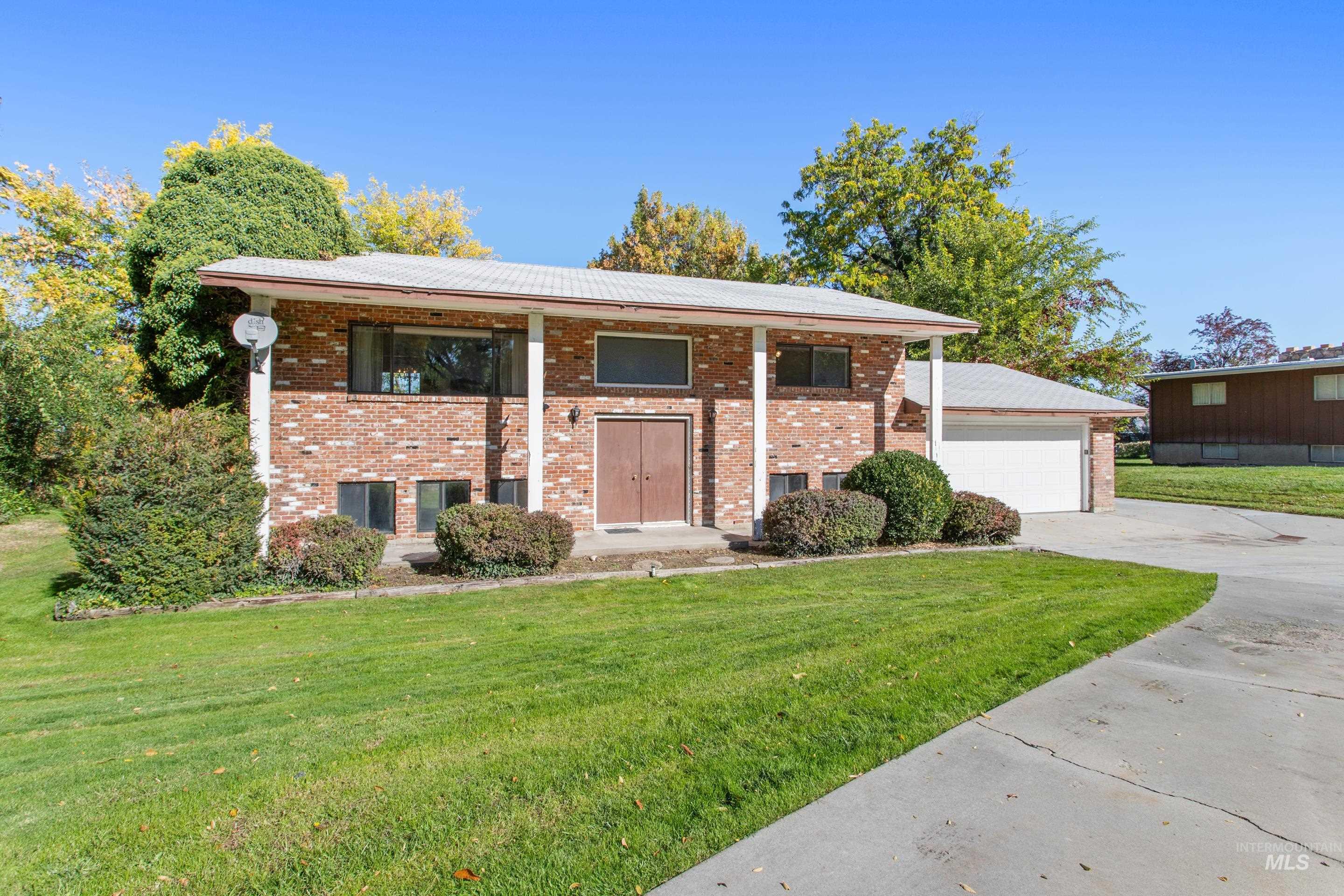 Bi-level home with a front lawn, brick siding, covered porch, and a garage
